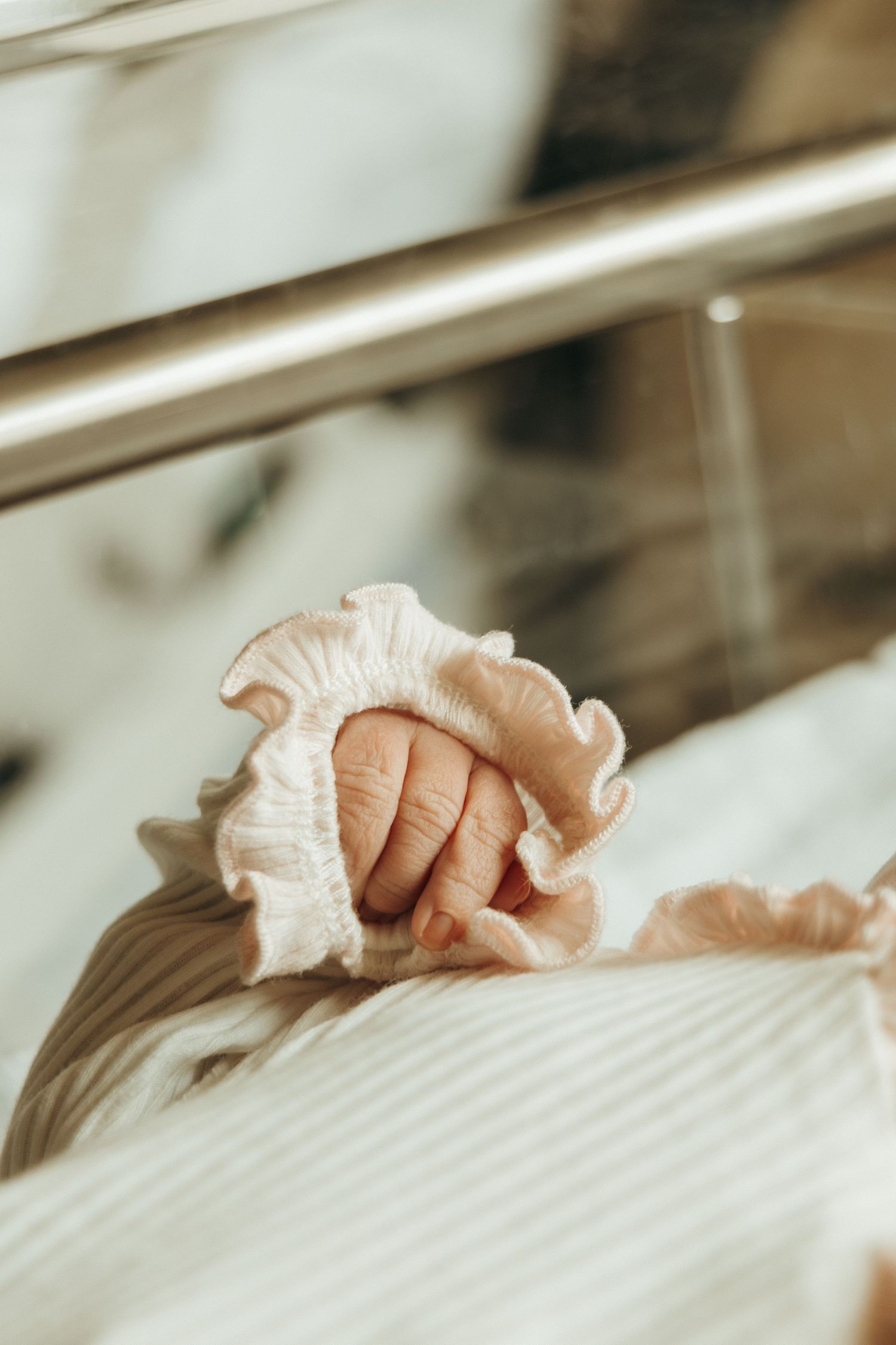 Close-up view of tiny newborn fingers clutching white fabric in soft lighting.