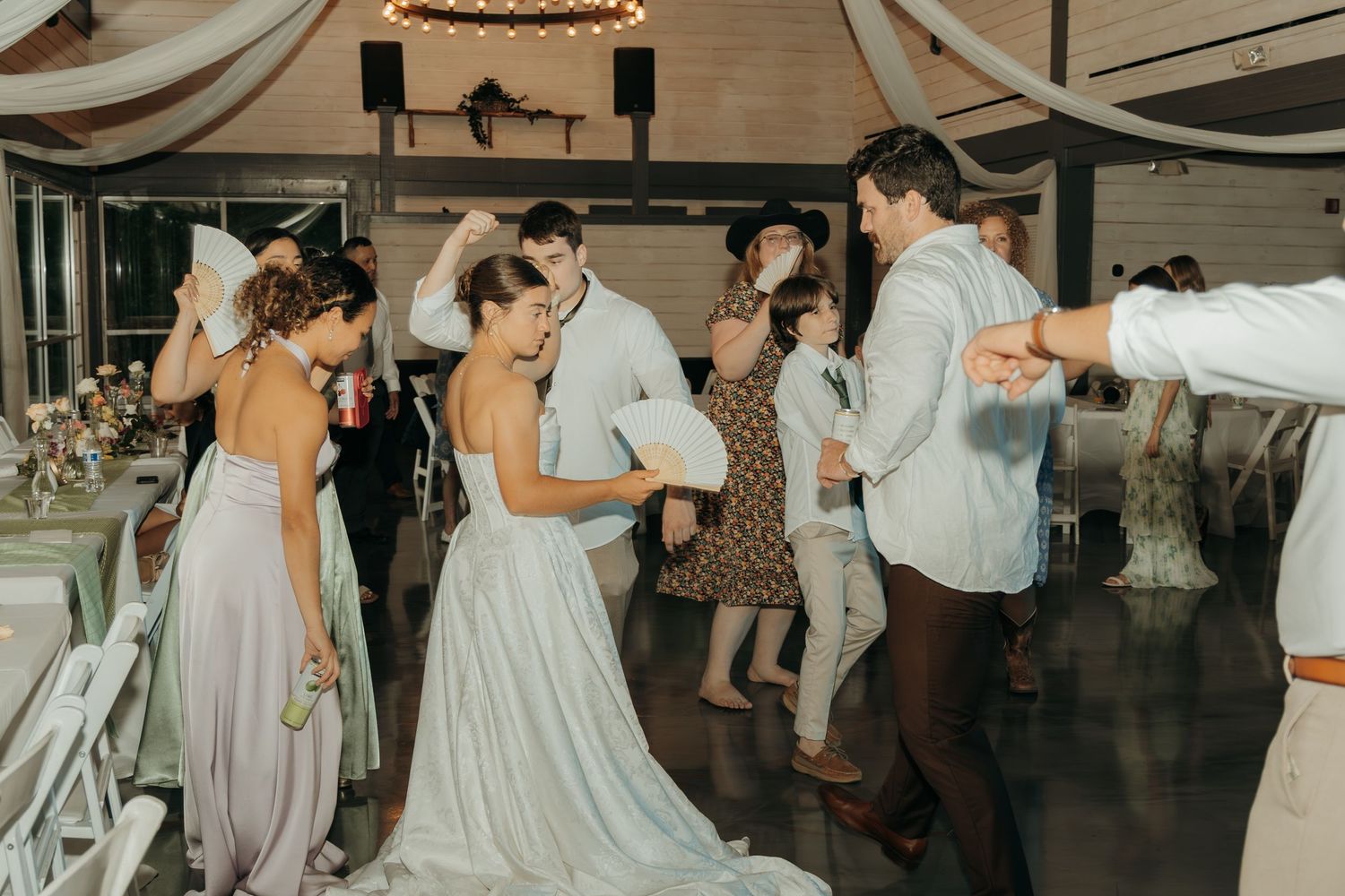 Wedding reception guests dancing energetically on a wooden dance floor decorated with white fabric draping.