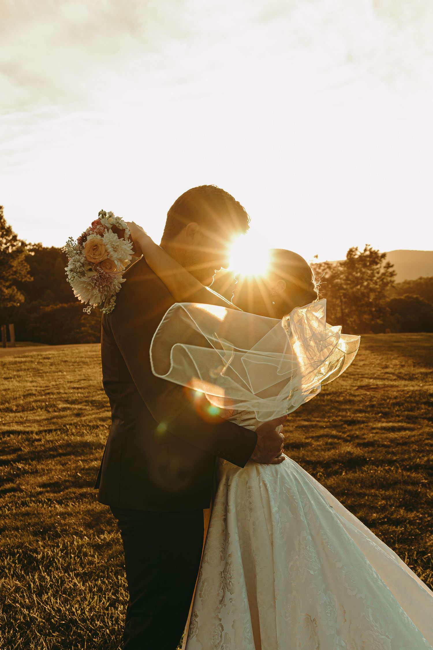 Romantic sunset wedding portrait showing a couple dancing in a golden field with flowing veil.