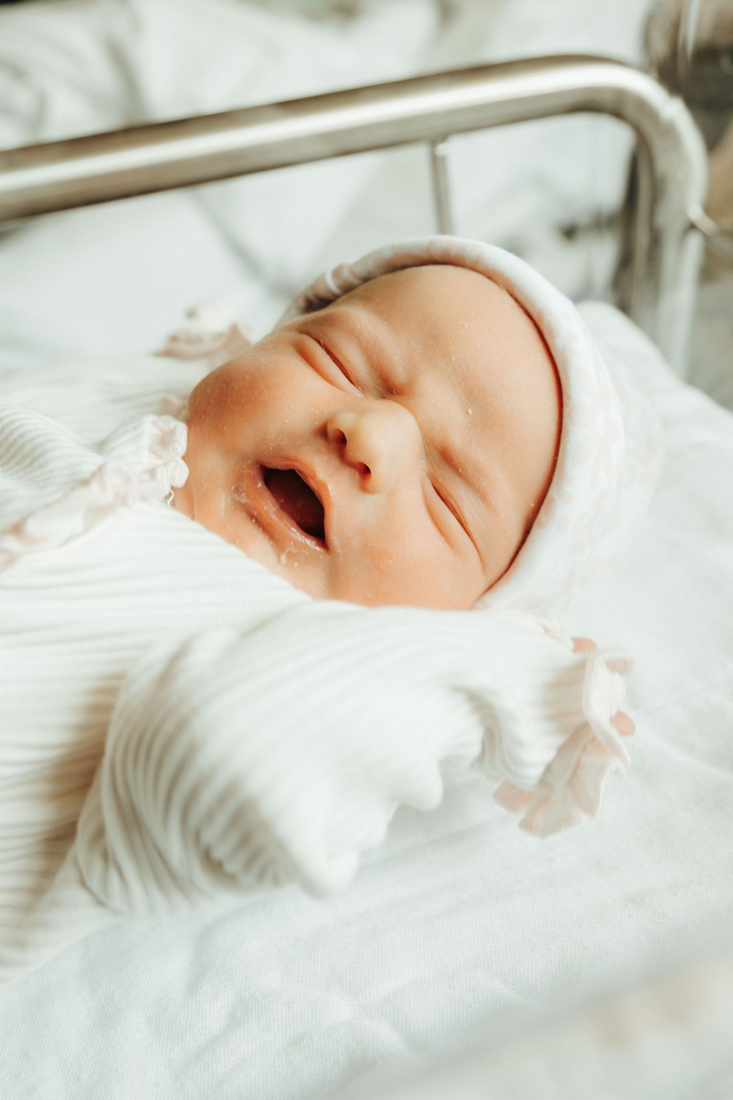 Sleeping newborn wearing white clothing on white bedding in gentle natural light.