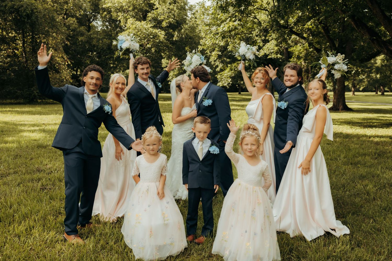 Wedding party members in formal attire walk together on grassy lawn during outdoor celebration.