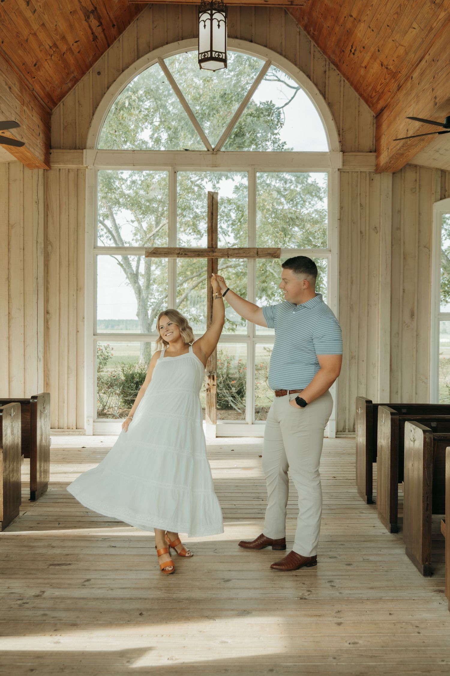 A couple dances together in a rustic wooden gazebo with arched windows and natural lighting.