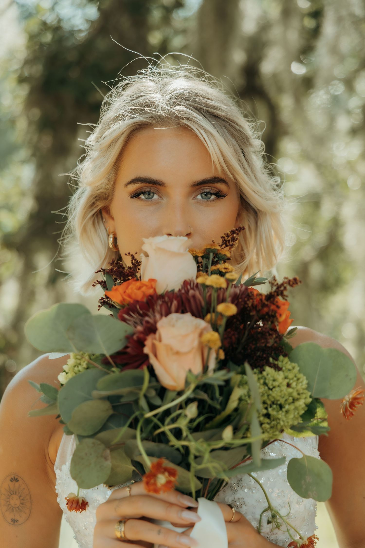 Beautiful autumn wedding bouquet with peach roses, burgundy dahlias and eucalyptus leaves in outdoor sunlit setting.