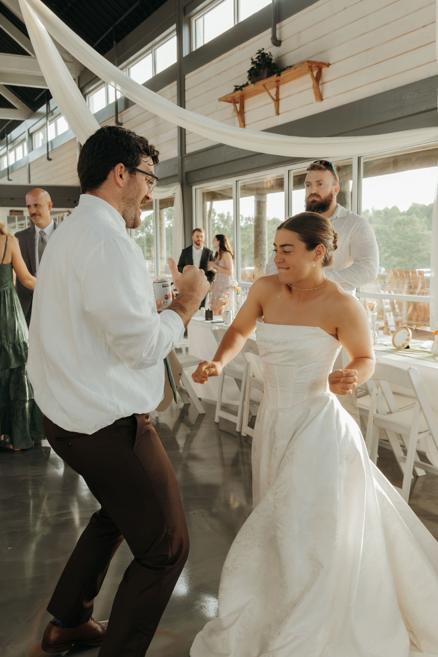 Wedding couple dancing energetically in a bright indoor reception venue with white draping.
