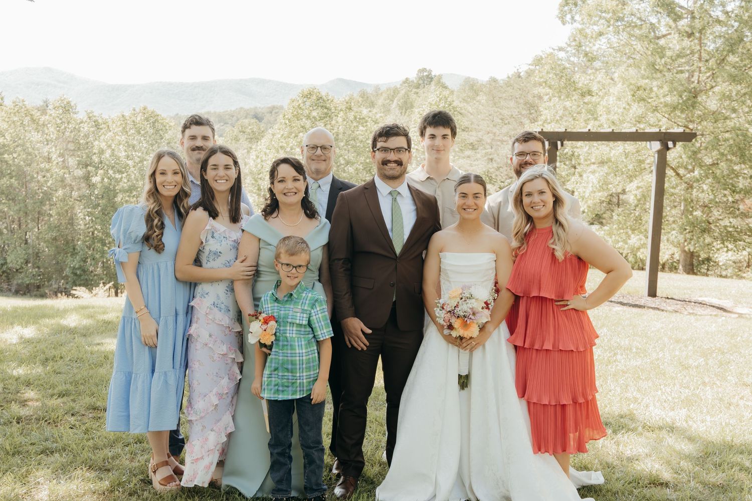 Small wedding party poses together on a hilltop with mountain scenery in the background.