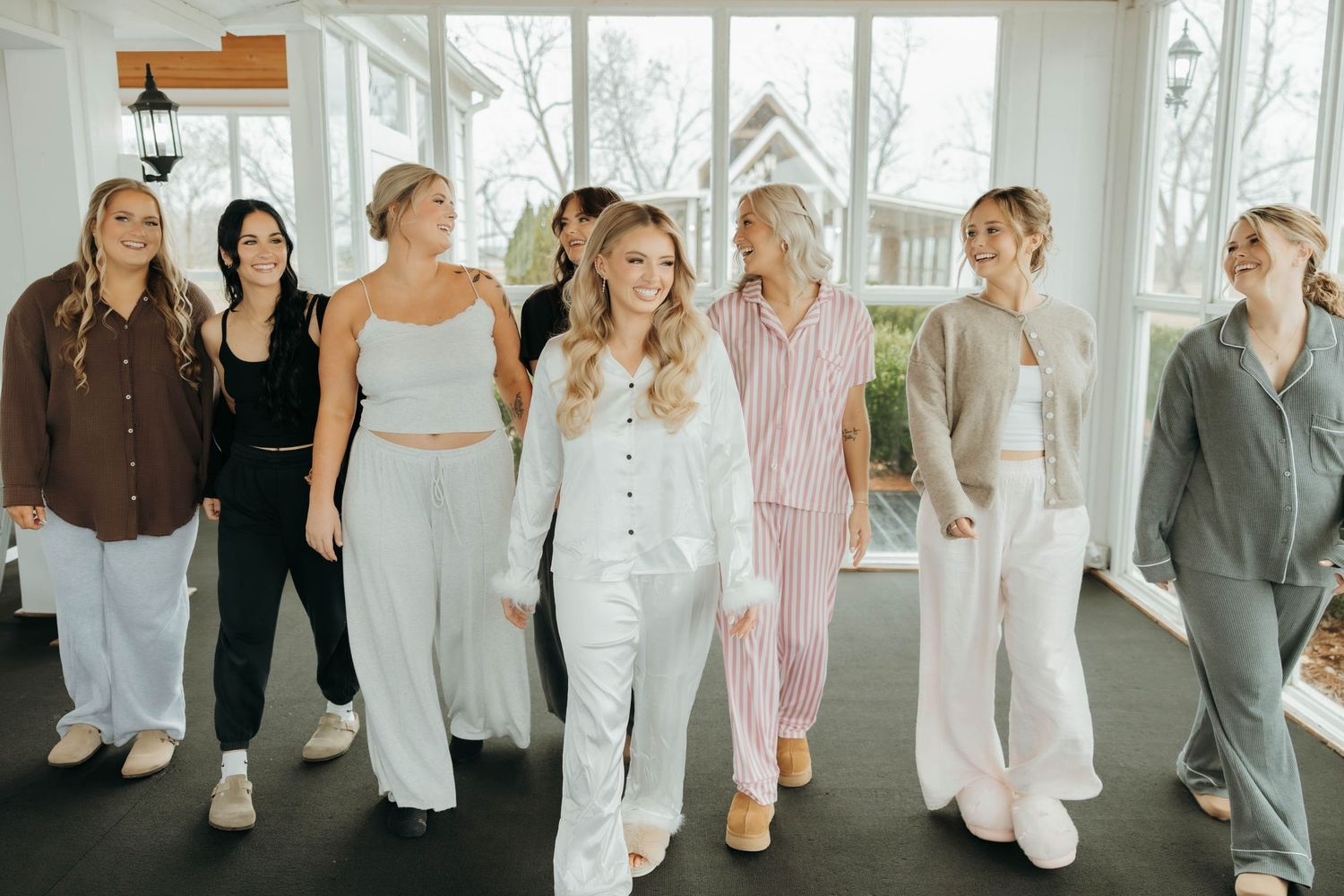 A group of people wearing coordinated white outfits pose together in a bright sunlit room with large windows.