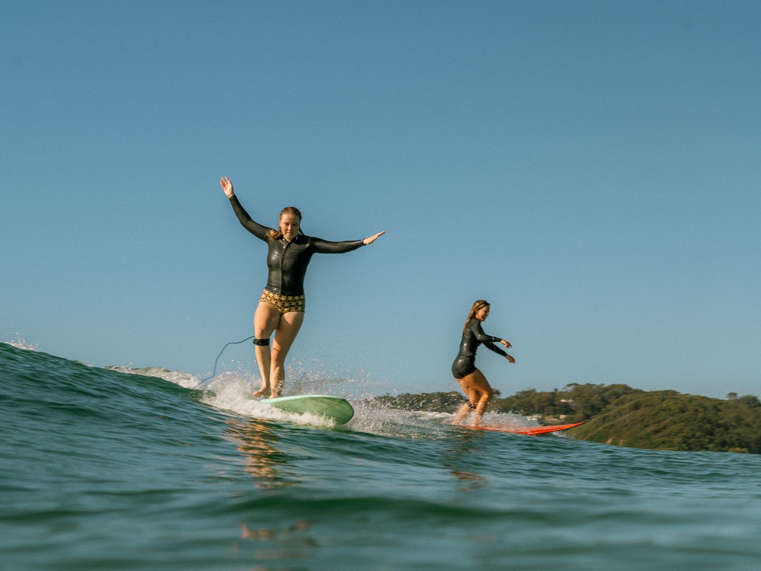 two female best friends surfing a wave together on their longboards with big happy smiles at Dudley, Newcastle NSW on a summer morning