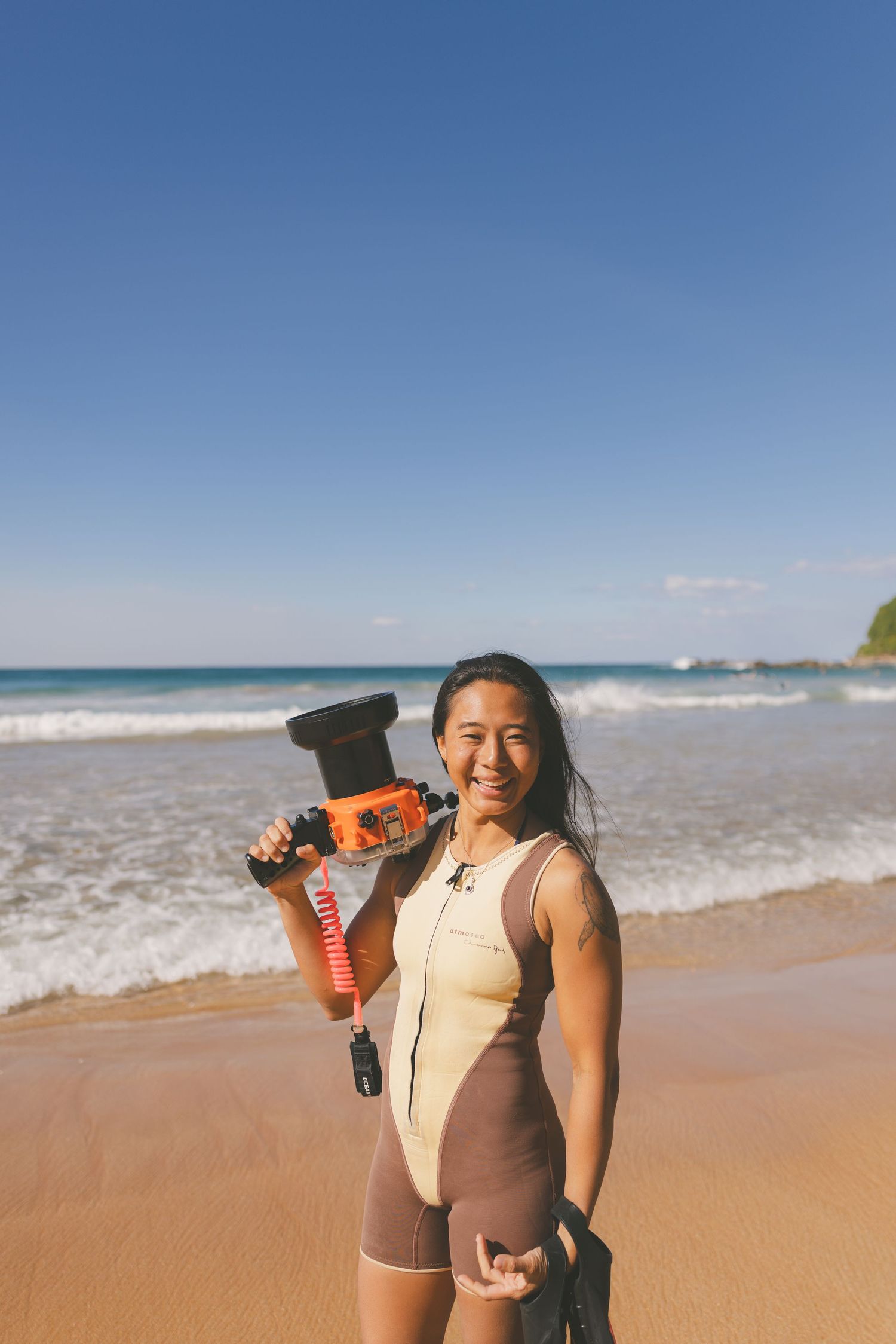 photo of Kanari posing with an underwater camera housing smiling at the camera in the summer wetsuit by the surf in Newcastle, NSW AUS