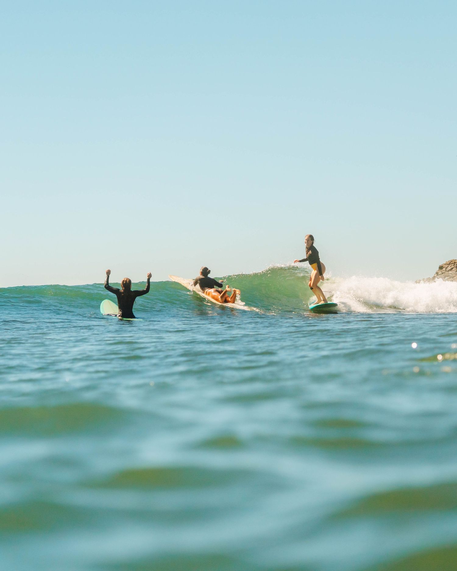 shot of one female surfer on a wave smiling and other woman sitting on the longboard cheering at Crescent Head, NSW with Sunlight Surfers