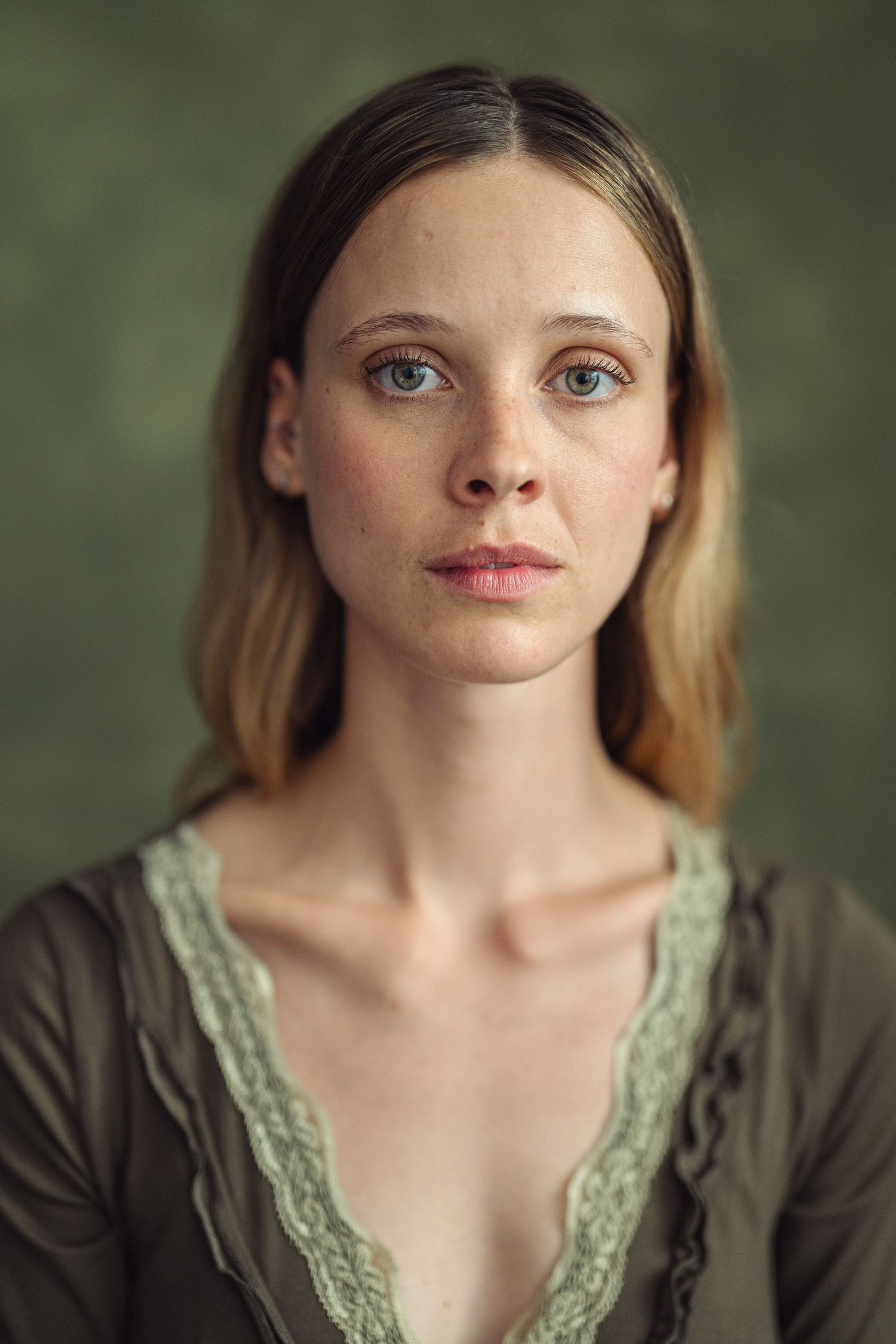 Young woman with blue eyes, freckles, and blonde hair wearing a green lace top poses for a portrait.
