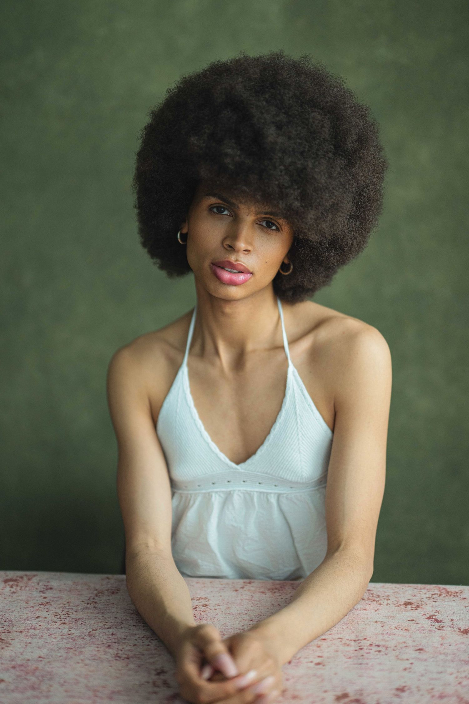 A person with natural afro hair wearing a white tank top poses against a green background in an artistic portrait series.