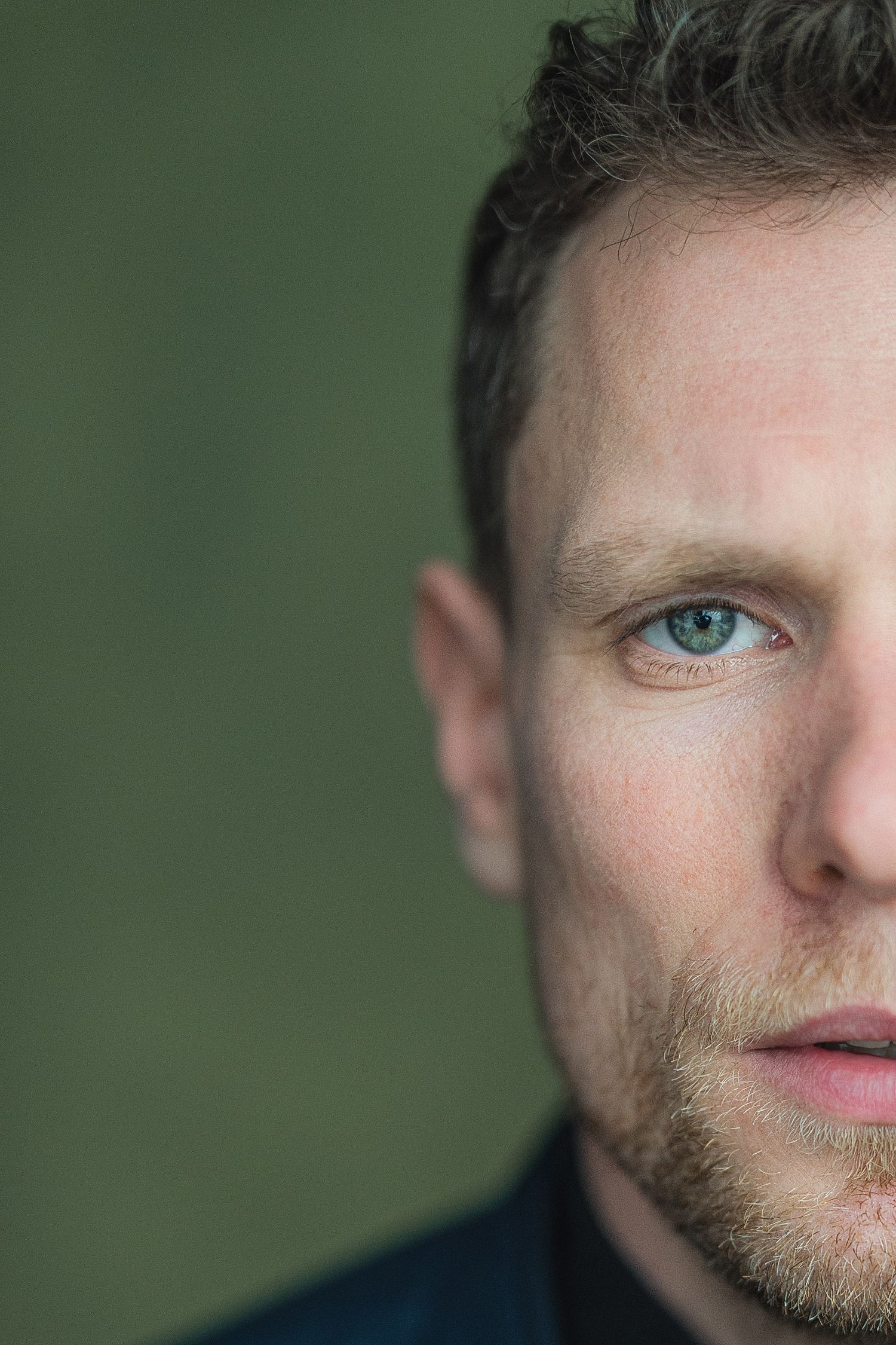 Close-up portrait against green background showing partial facial features with blue eyes and facial hair.