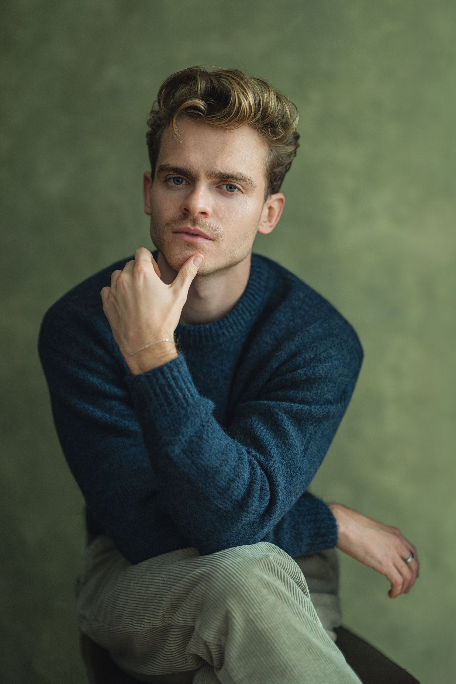 A series of four portraits showing someone in a navy blue sweater against a green background in contemplative poses.