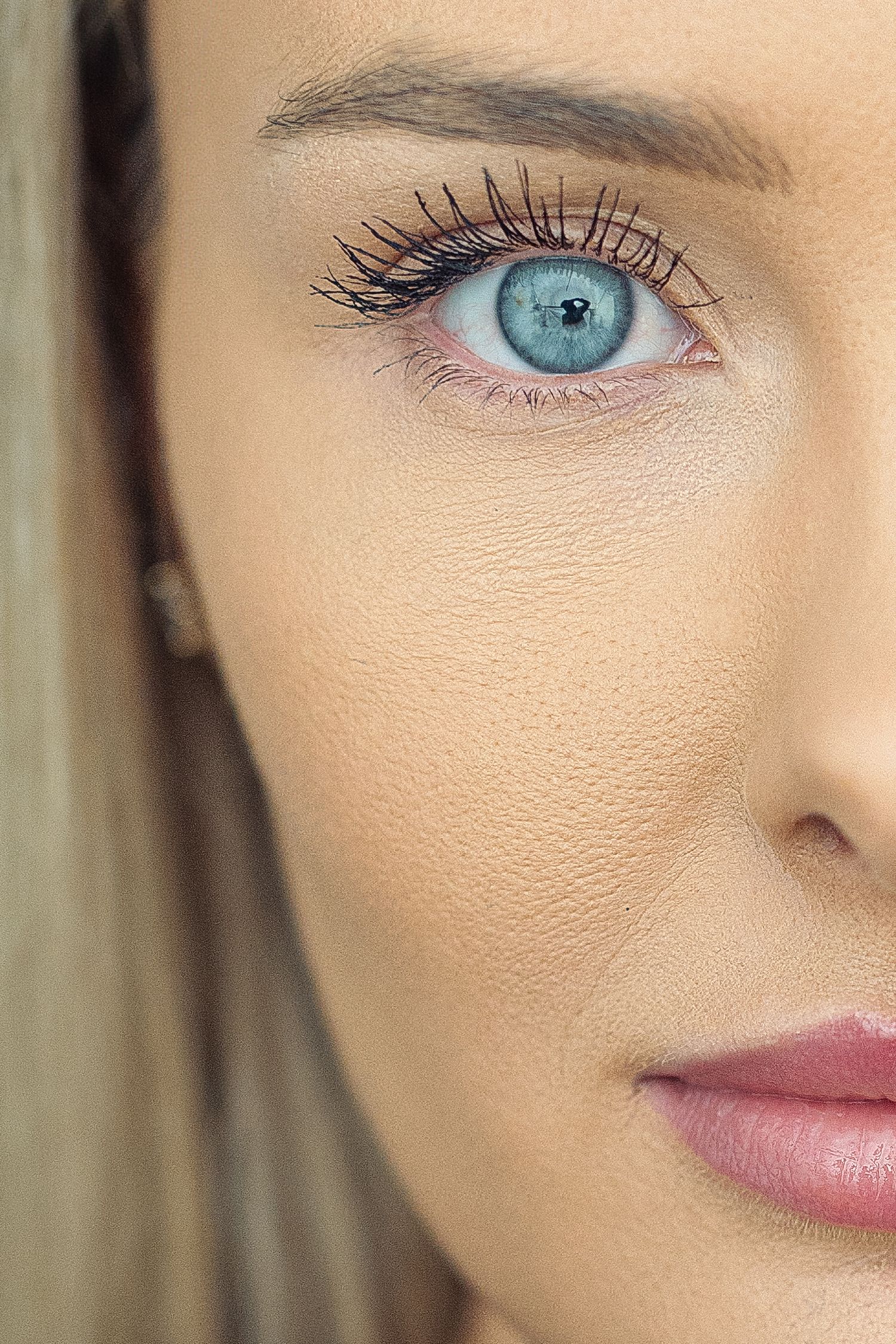 Close-up portrait of a woman with striking blue eyes, long lashes, and pink lips wearing natural makeup.