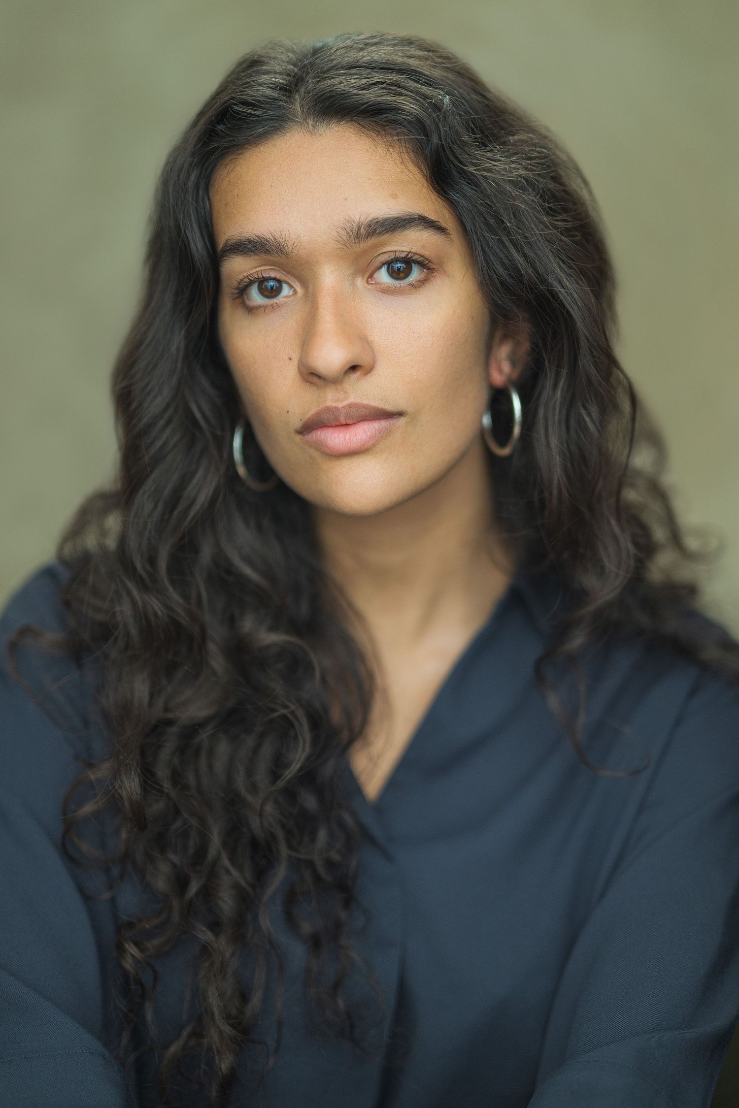 A person with long dark curly hair wearing a navy blue hoodie poses in a series of casual portraits against a neutral background.