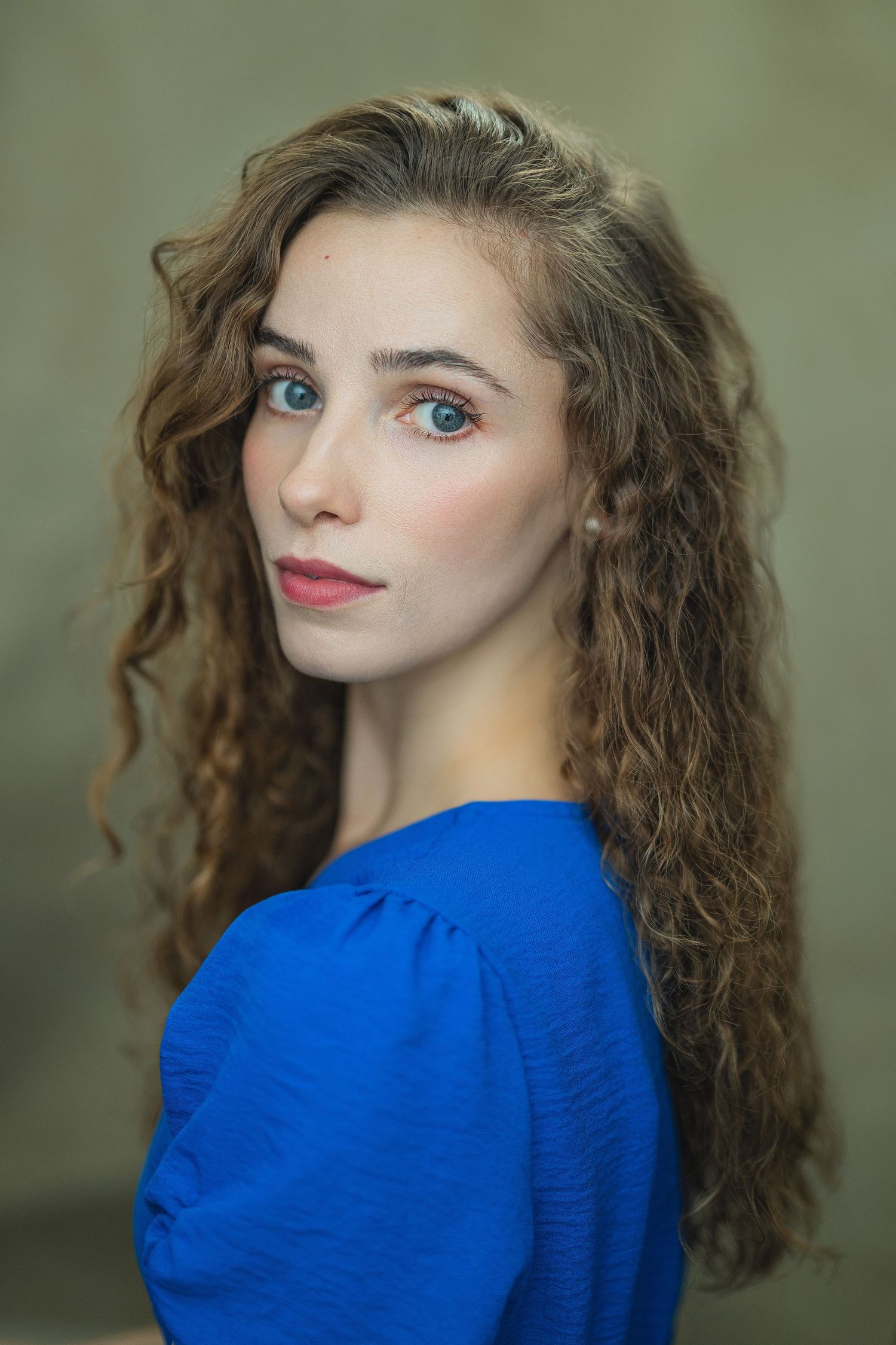 Portrait of a person with long wavy brown hair wearing a vibrant royal blue top against a neutral background.