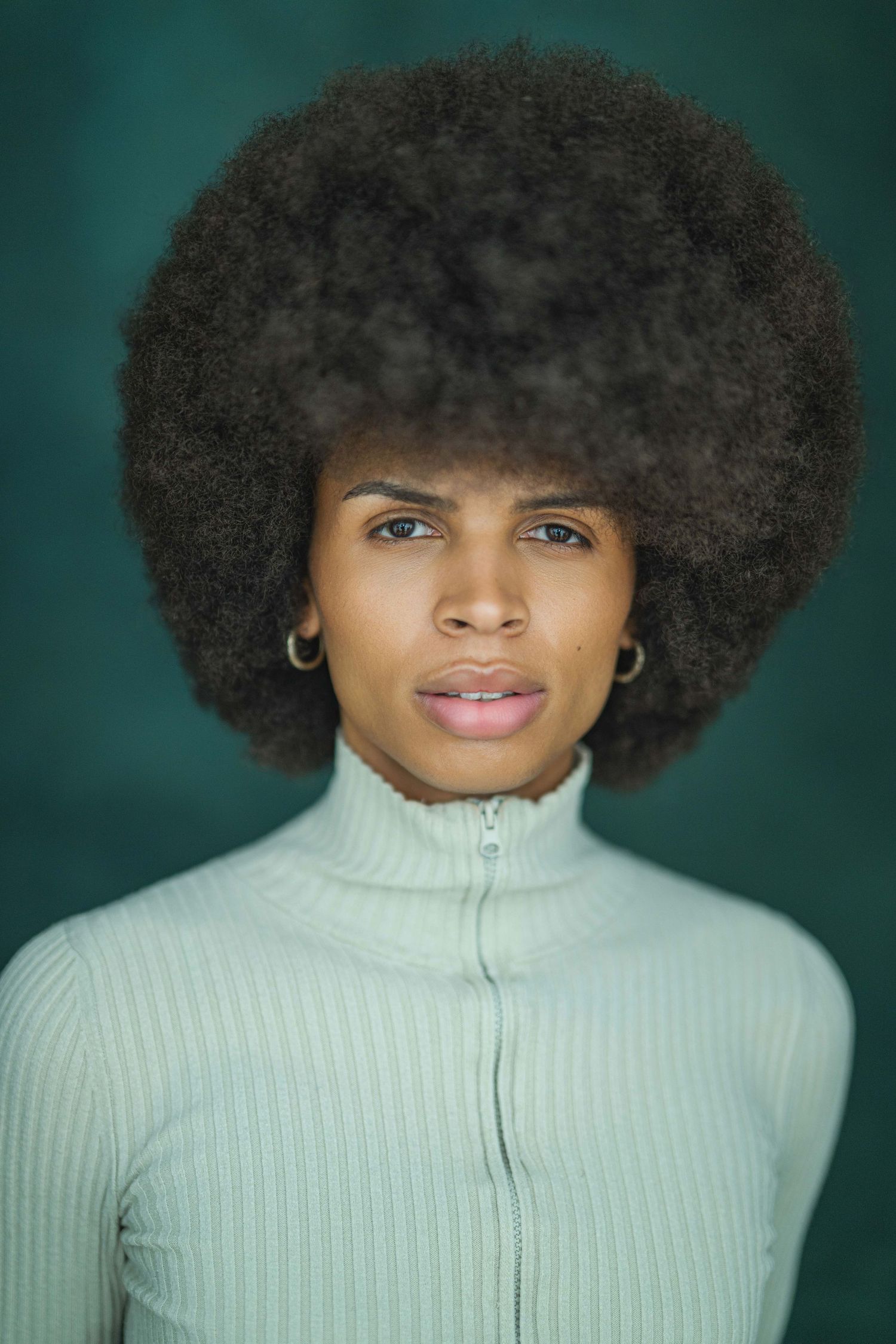 A series of portraits showing someone with a natural afro hairstyle wearing a white turtleneck sweater against a dark green background.