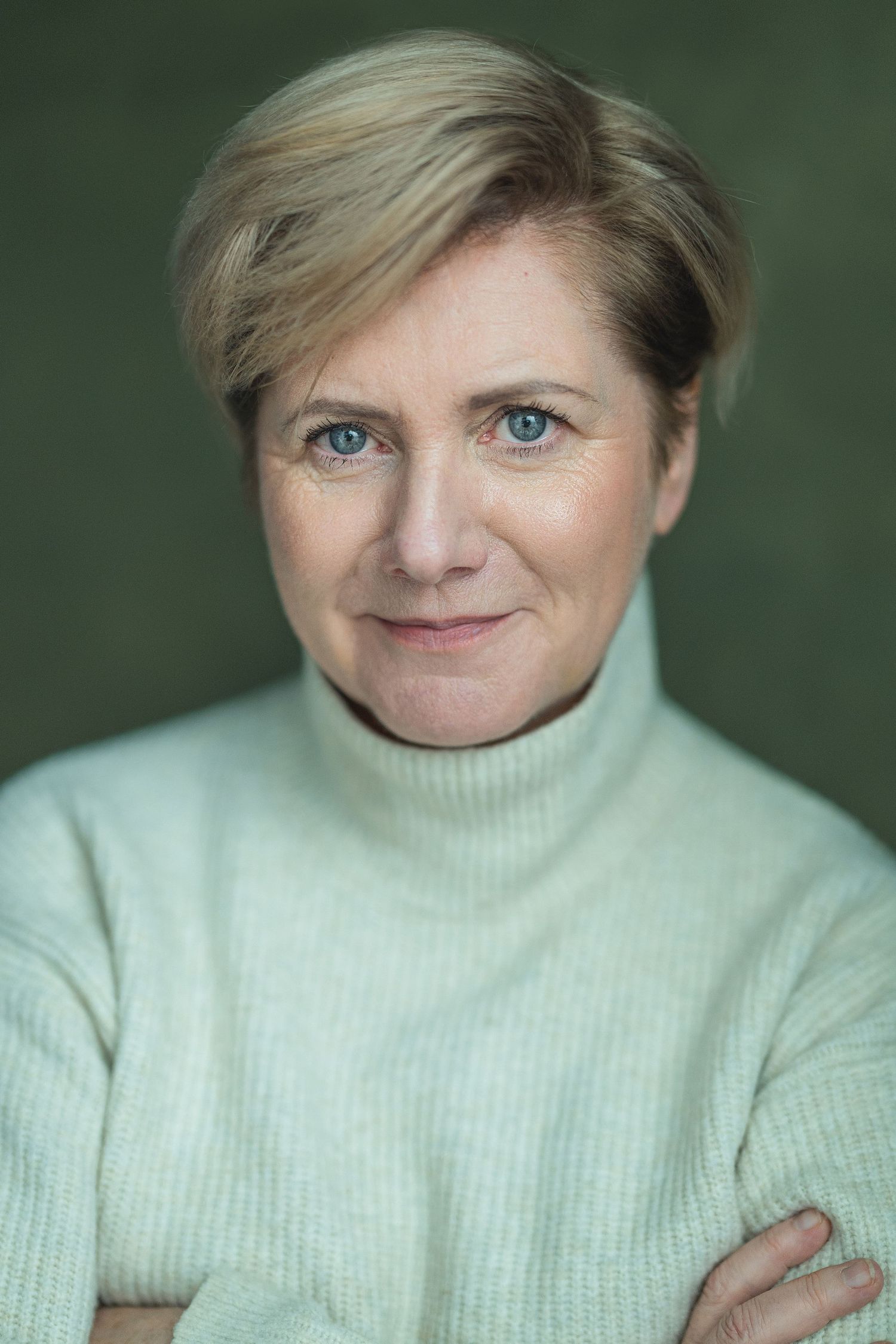 Professional headshot portrait of someone wearing a cream turtleneck sweater against a green background.