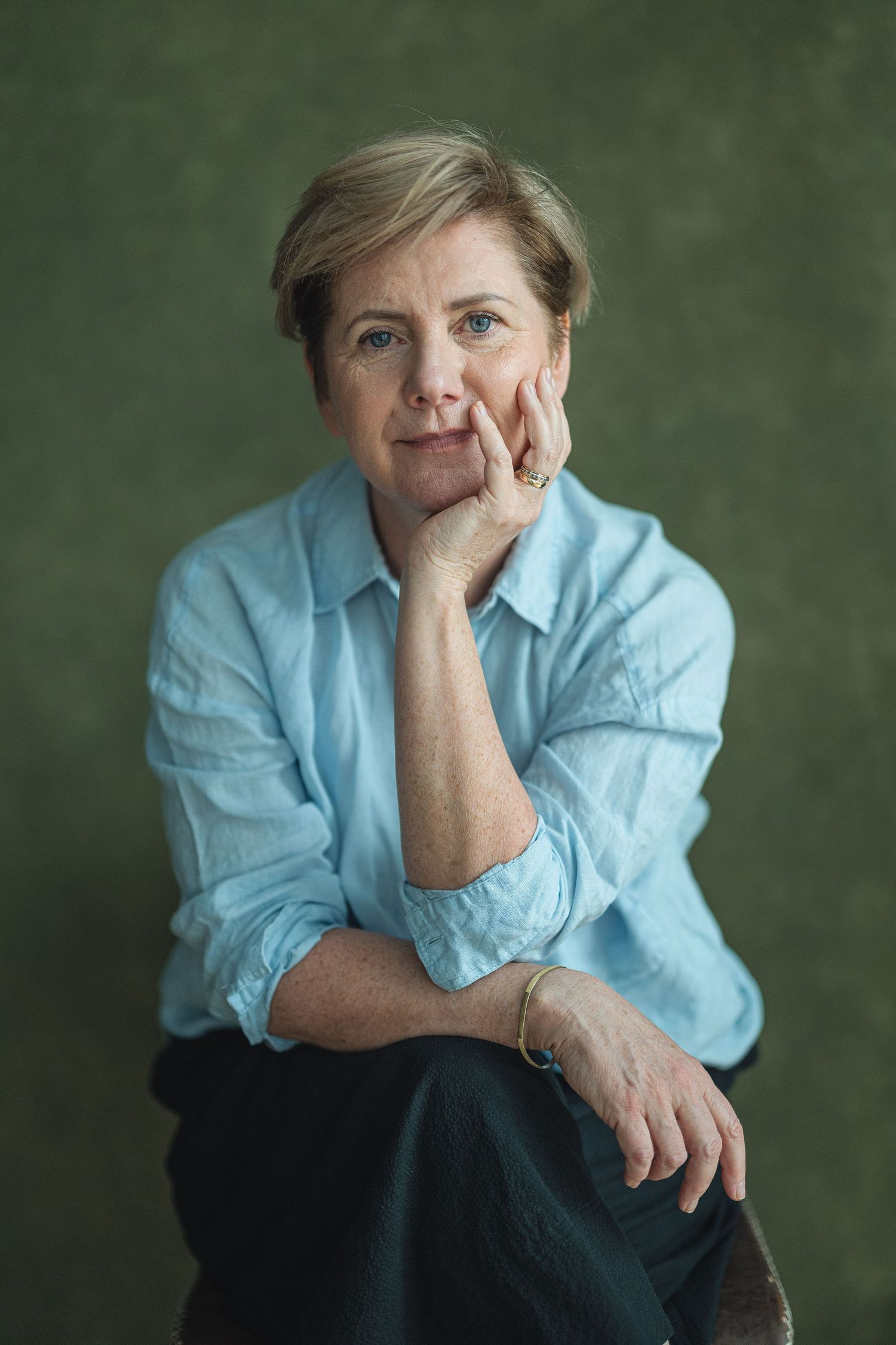 A series of five portraits showing someone in a light blue shirt against a dark green background posing thoughtfully.