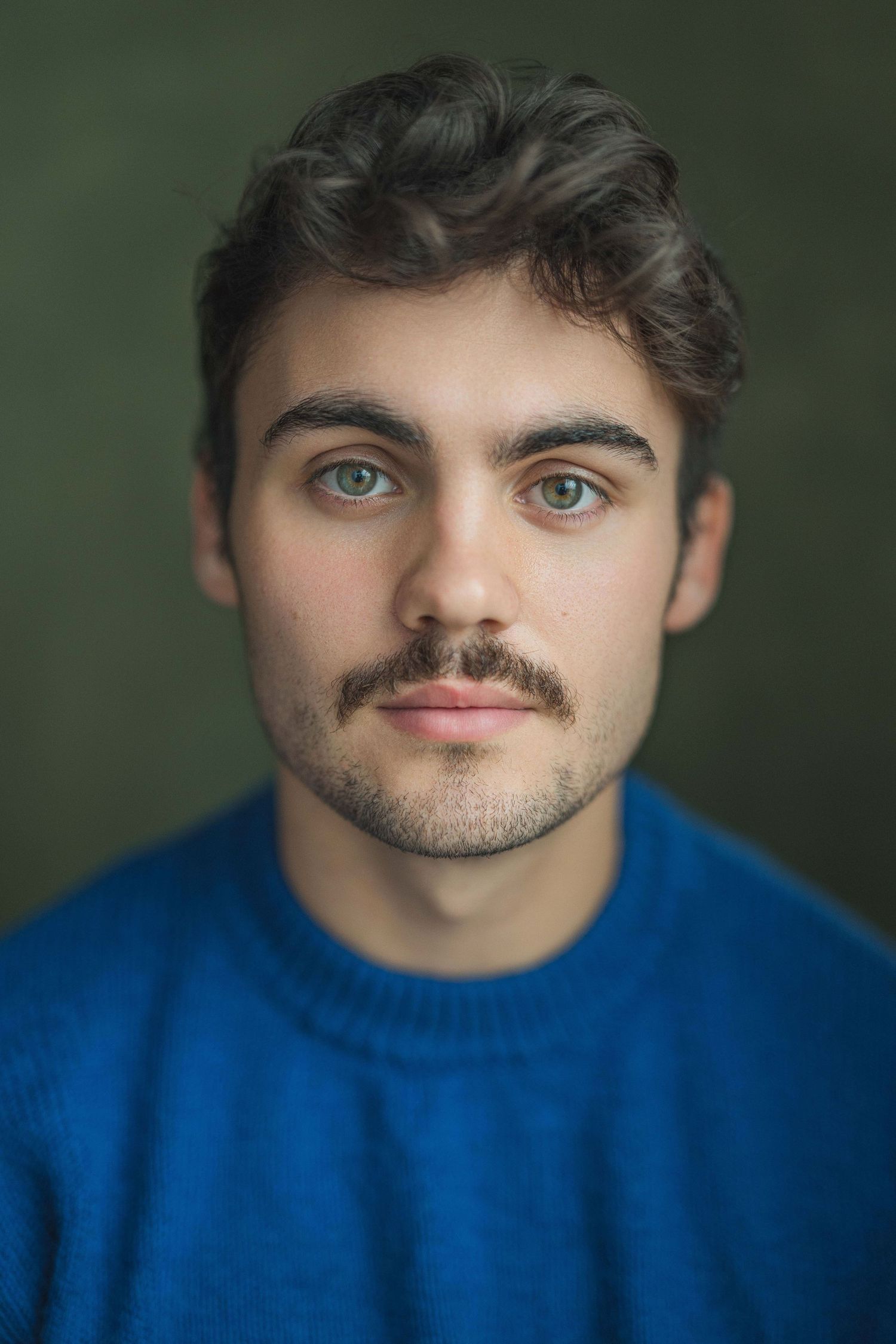 Portrait sequence showing different expressions and angles of someone wearing a bright blue sweater against a dark green background.