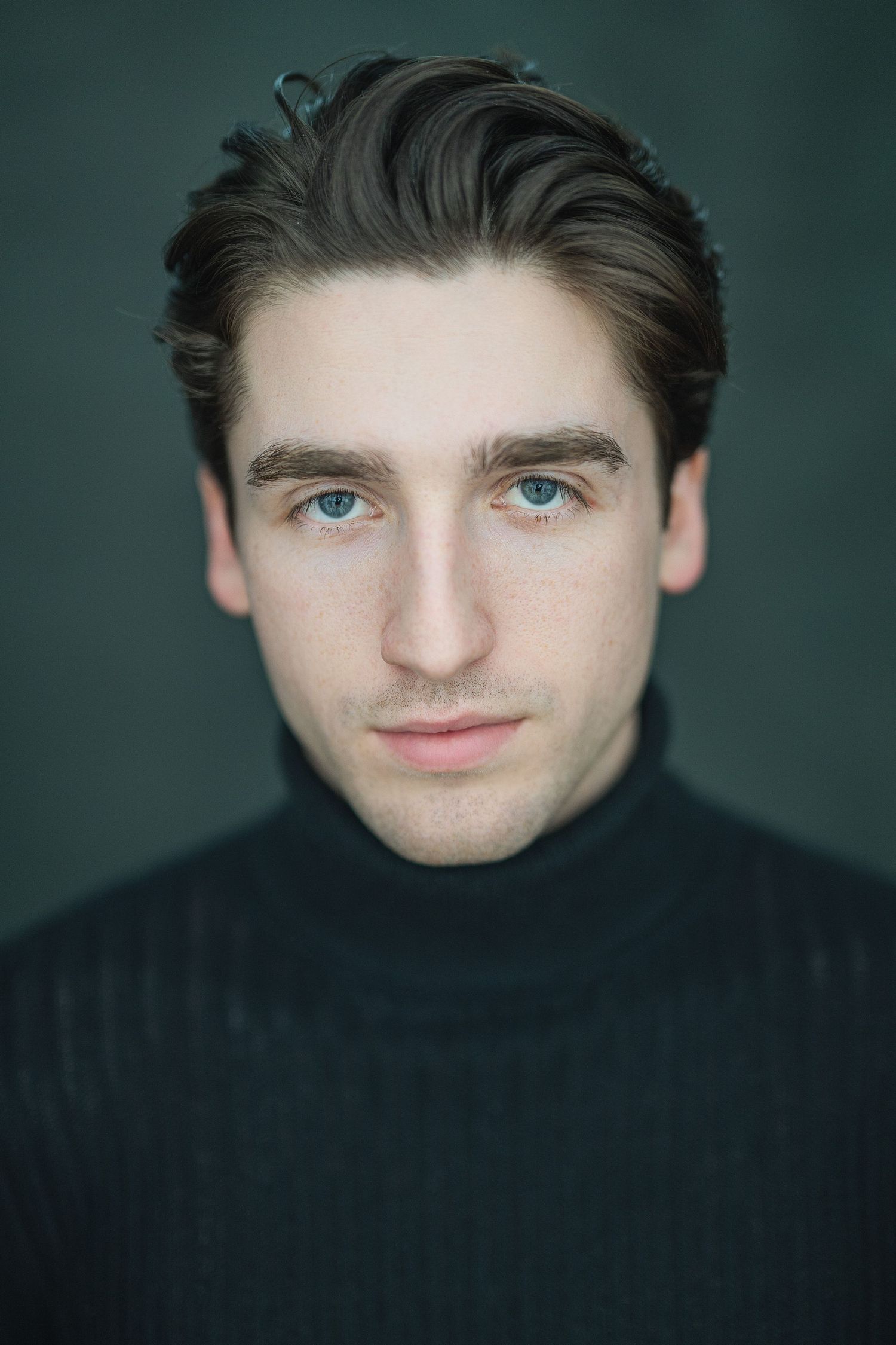 Portrait of someone wearing a black turtleneck sweater against a dark green background.
