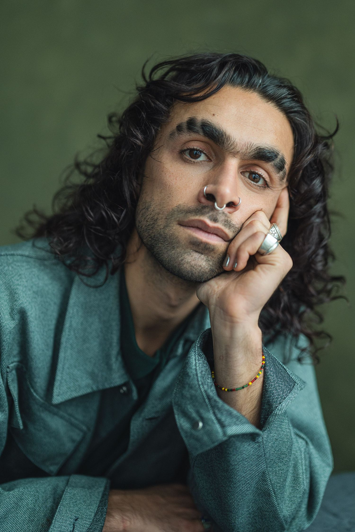 A series of four portrait photos showing someone in a teal sweater resting their head on their hand against a green background.