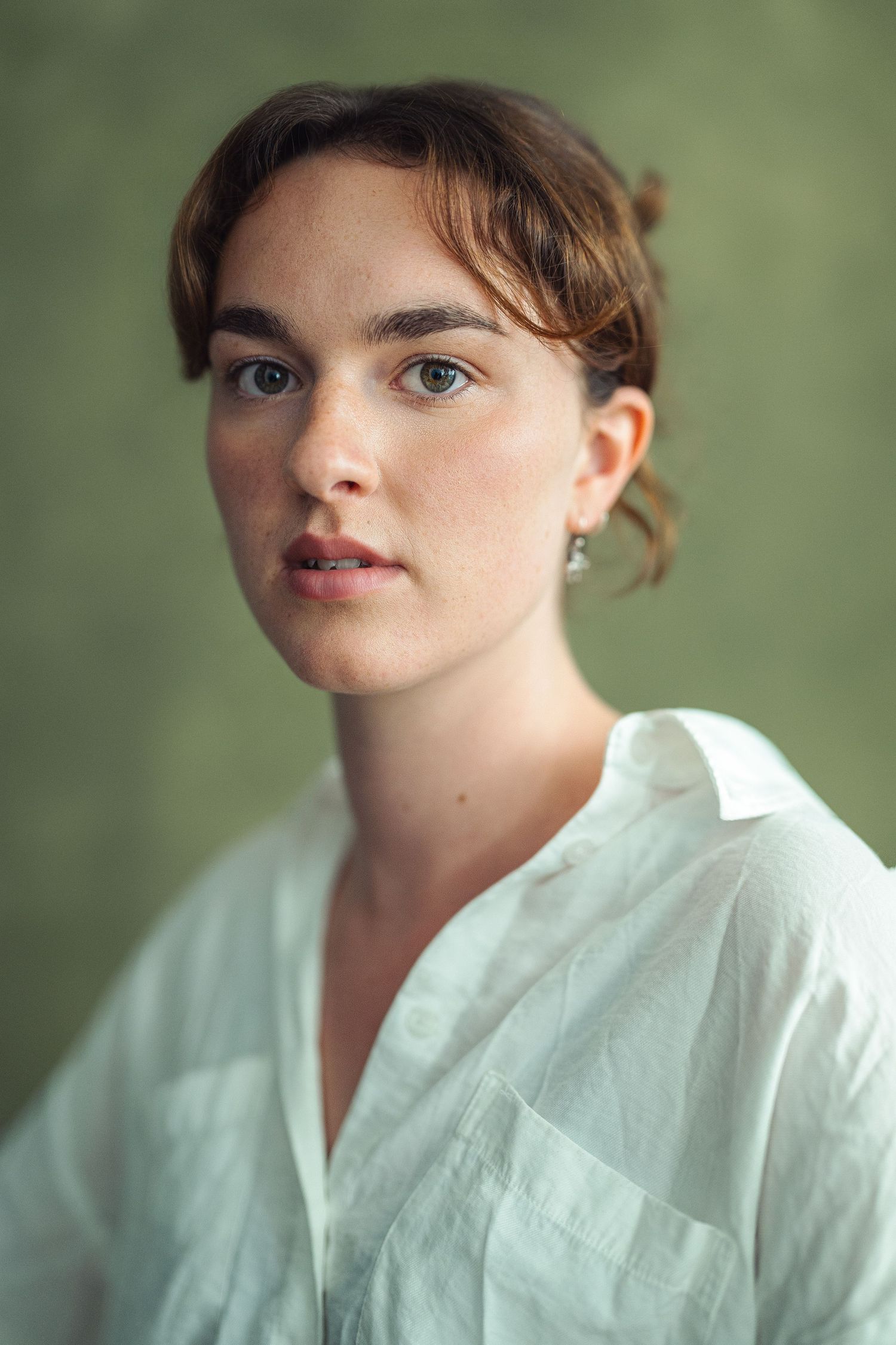 Young woman with auburn hair in white linen shirt poses against green background in natural portrait photo.