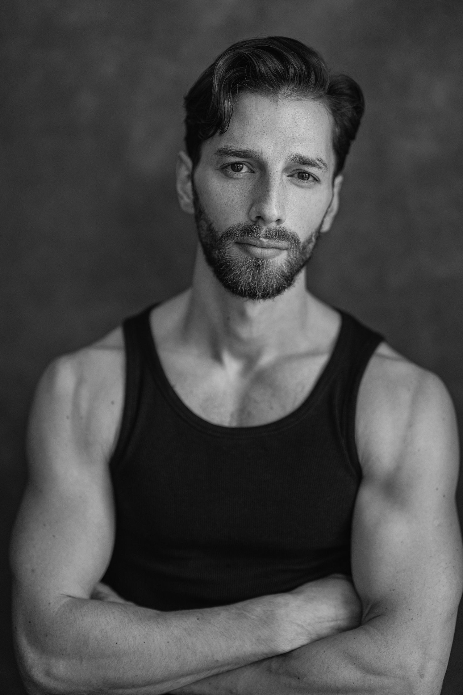 A black and white photo series showing a bearded man in a black tank top posing against a dark background.