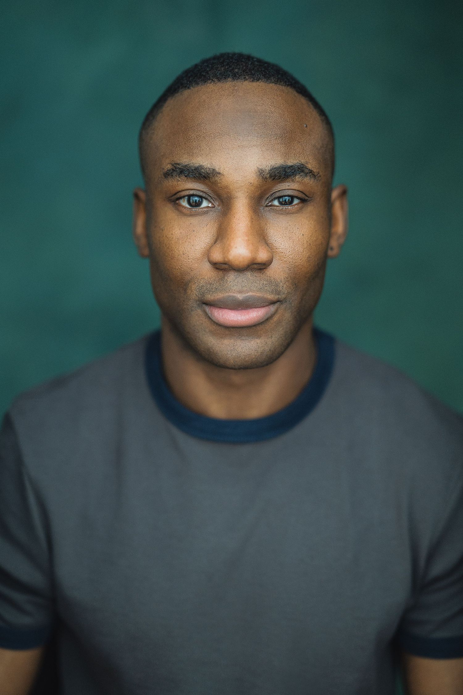 Professional headshot portrait against teal background showing warm smile and dark gray t-shirt.