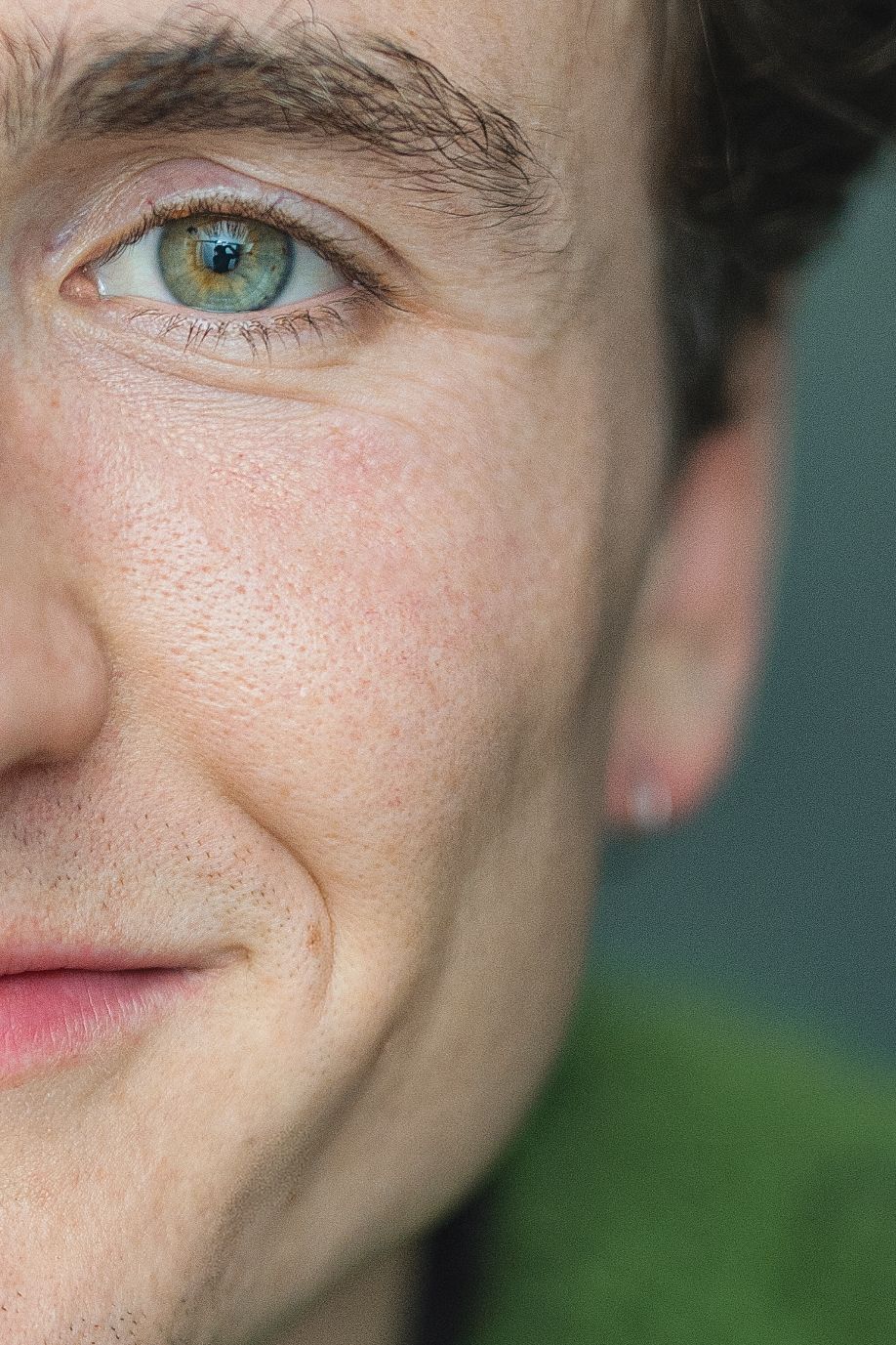Close-up photo of bright blue-green eyes and freckled skin against a blurred green background.