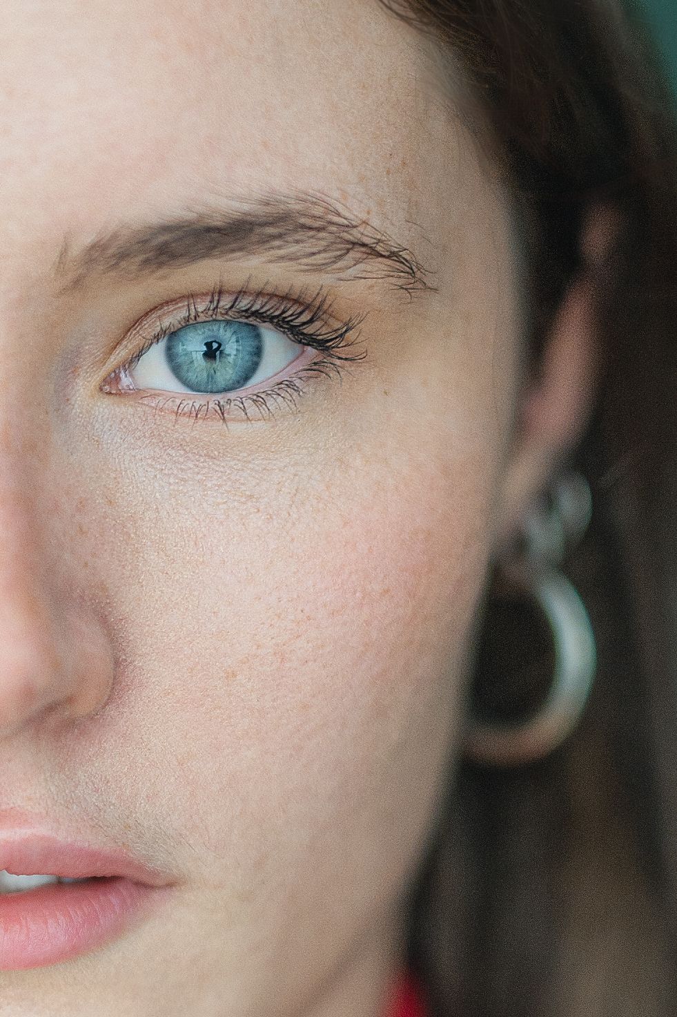 Close-up macro photograph of a bright blue eye with long eyelashes and a crescent-shaped silver earring visible.