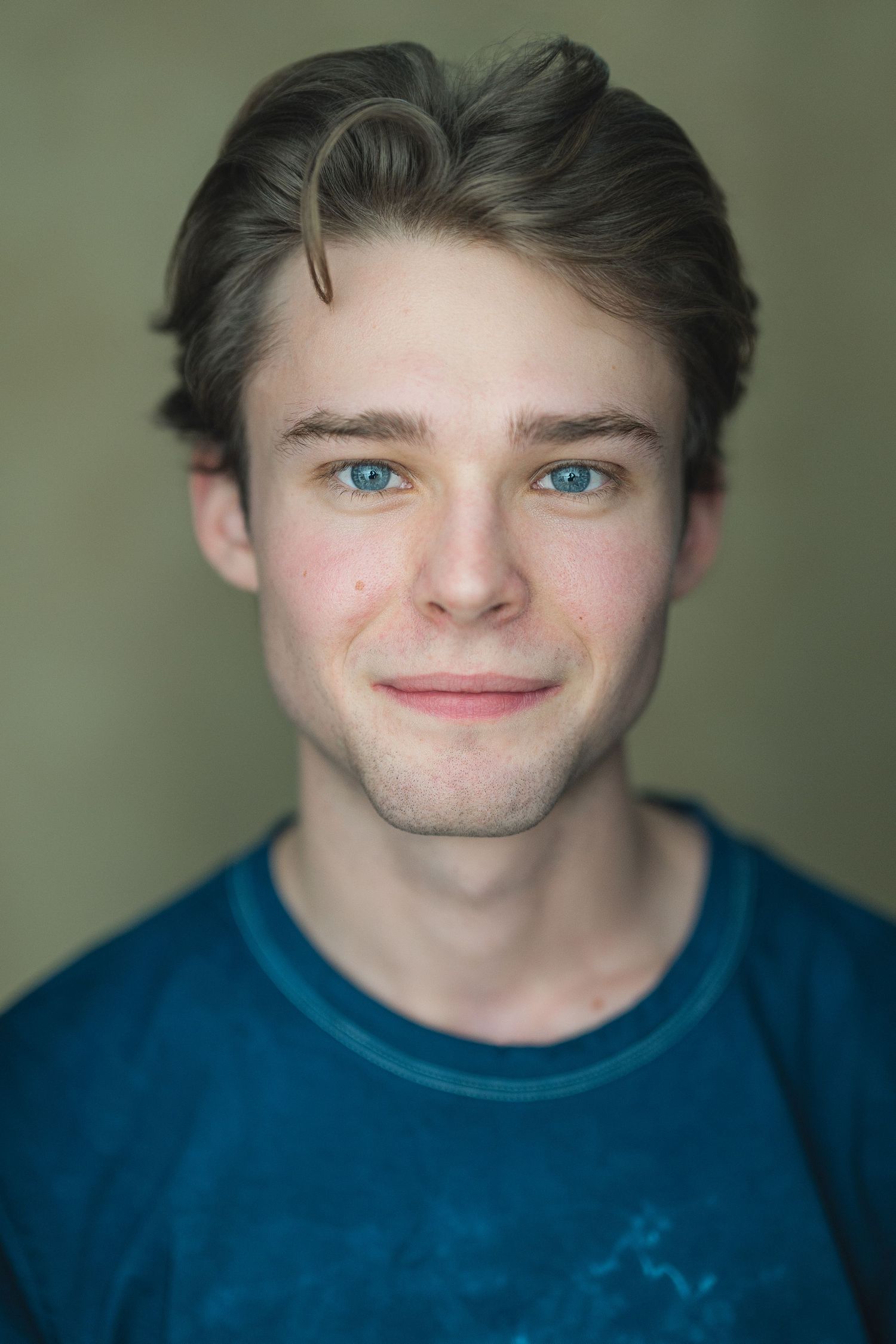 A young person with striking blue eyes and brown hair wearing a teal colored t-shirt against a neutral background.