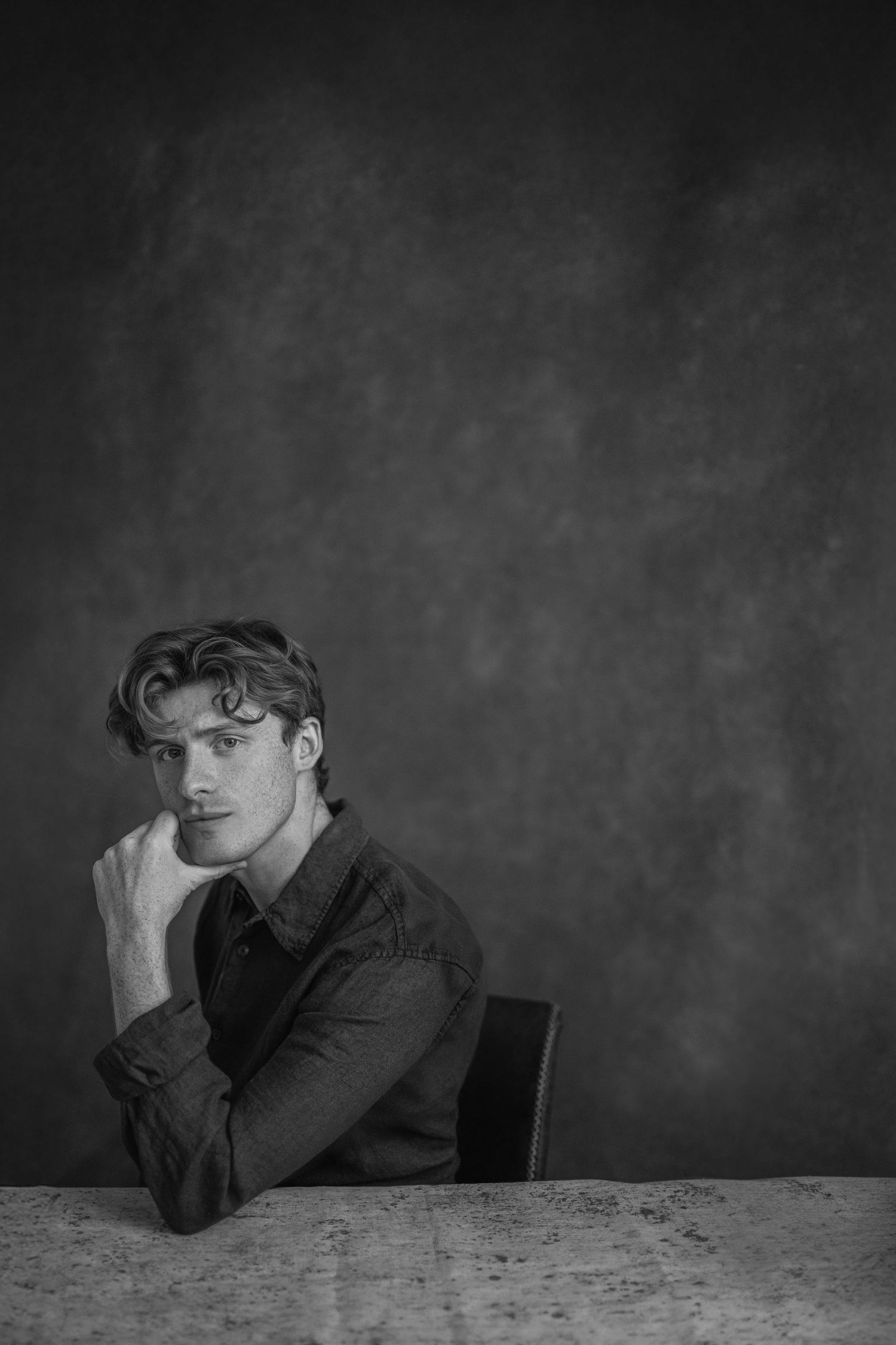 A dramatic black and white photo series showing someone in dark clothing resting their head on a table in contemplative poses.