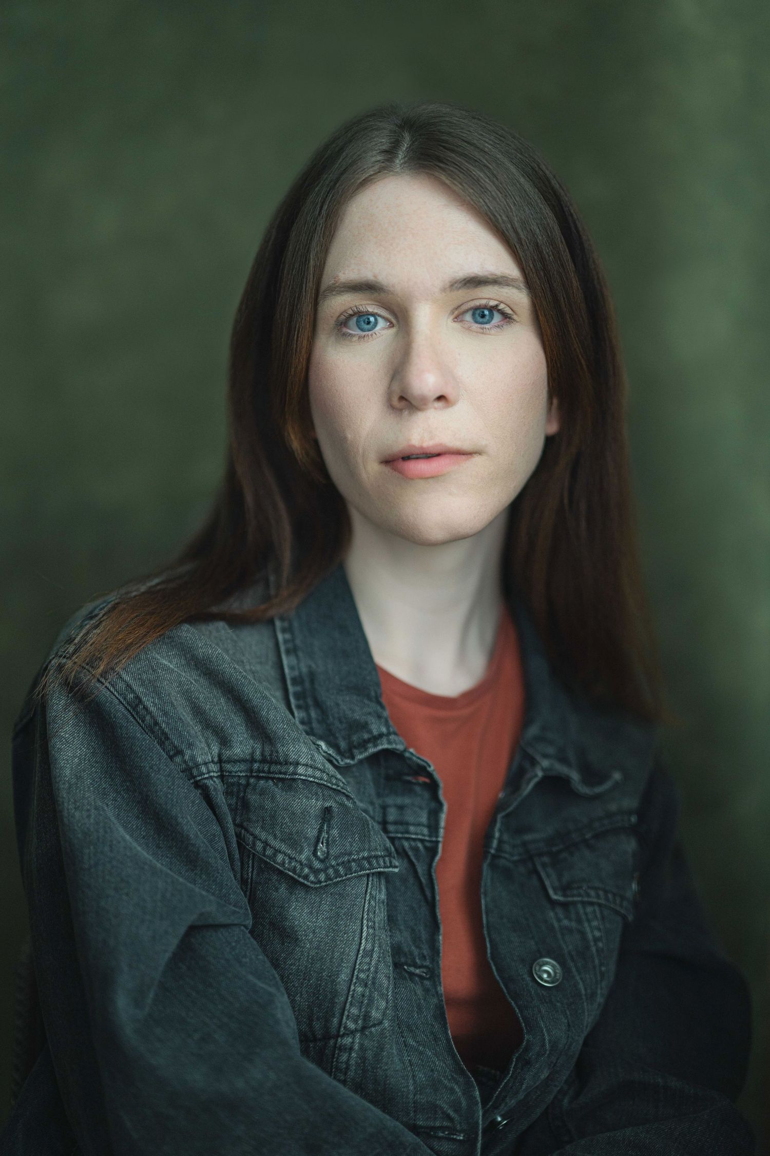 Young woman with blue eyes and long brown hair wearing a denim jacket over red shirt, portrait photo.