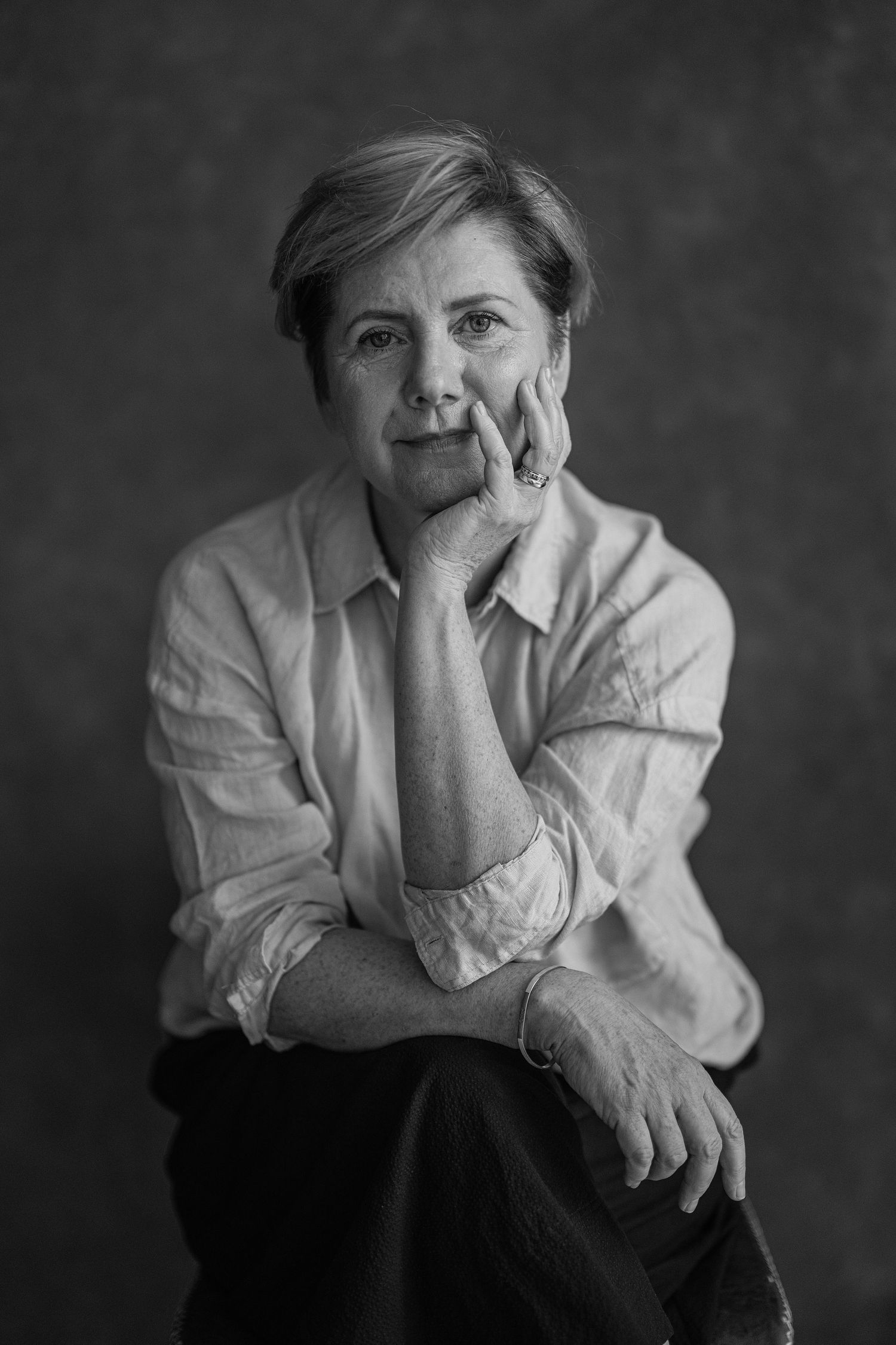Black and white portrait of a person in a white button-down shirt with hand resting thoughtfully on their chin.