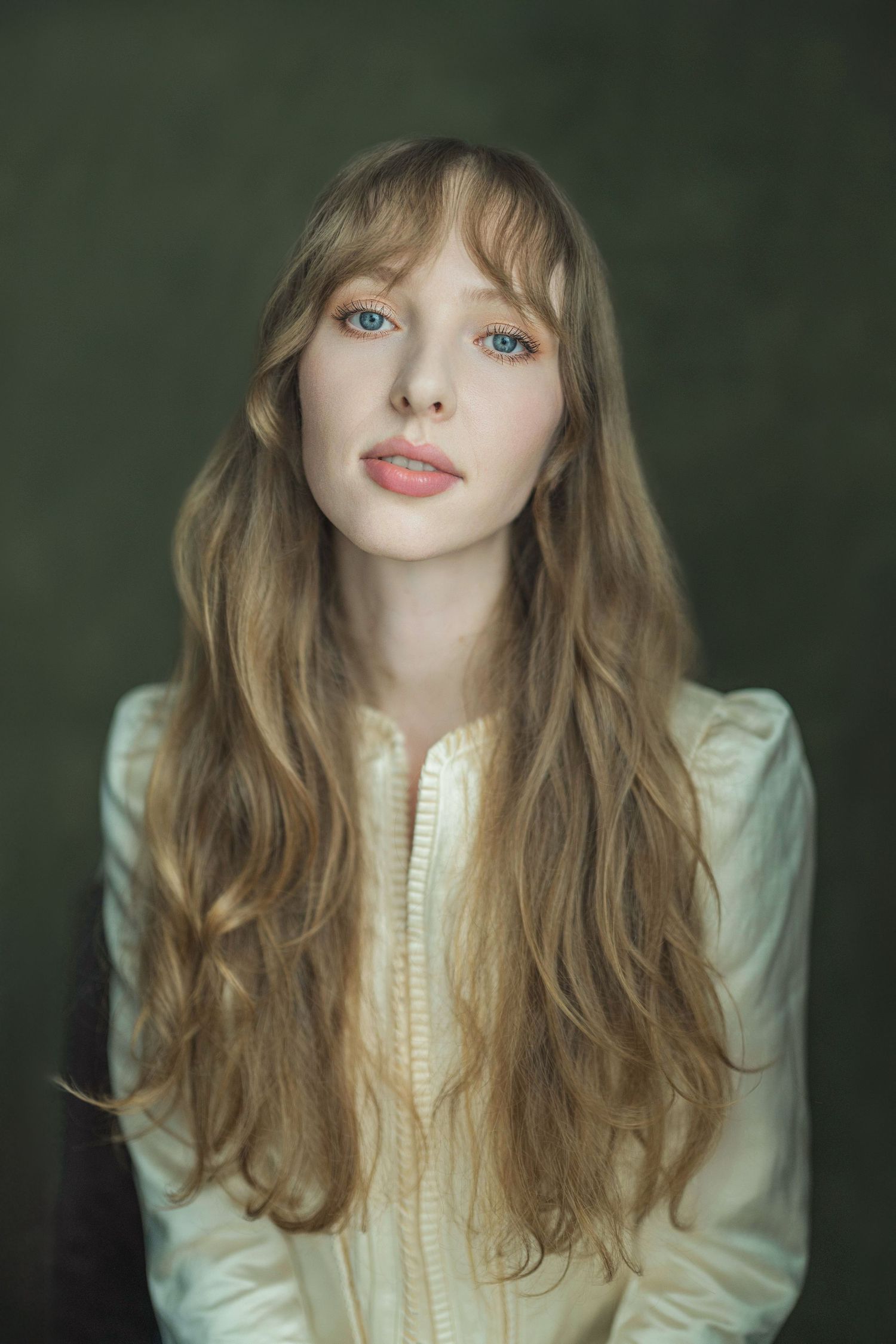 Portrait series showing someone with long wavy blonde hair wearing a cream colored blouse against a dark green background.