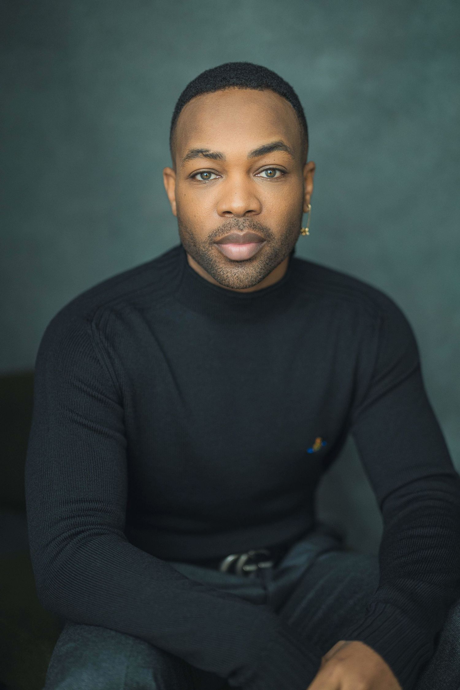 Professional studio portrait against a teal backdrop with a person wearing a black sweater.