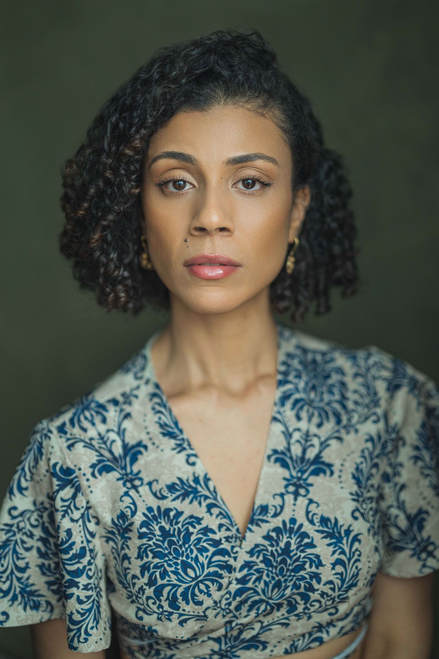 Portrait of someone wearing a white and blue floral patterned dress with natural curly hair against a dark background.