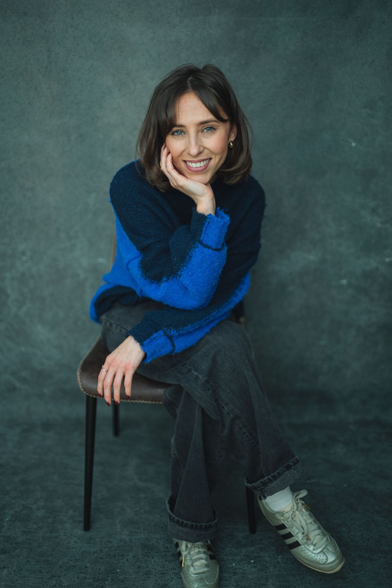 A series of four studio portraits showing someone in a blue sweater and jeans sitting casually on a dark background.