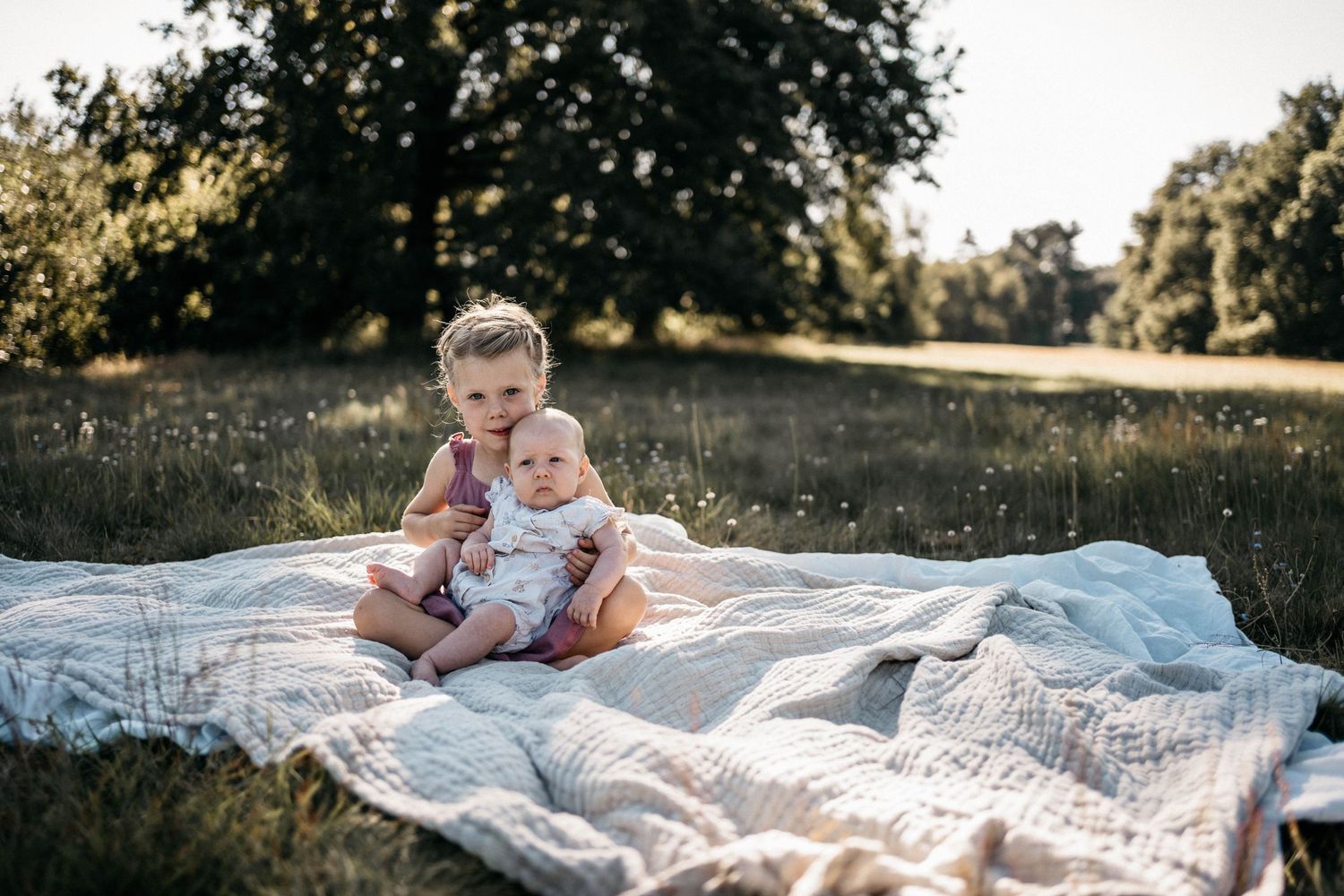 Children relaxing together on white picnic blanket in sunny meadow.