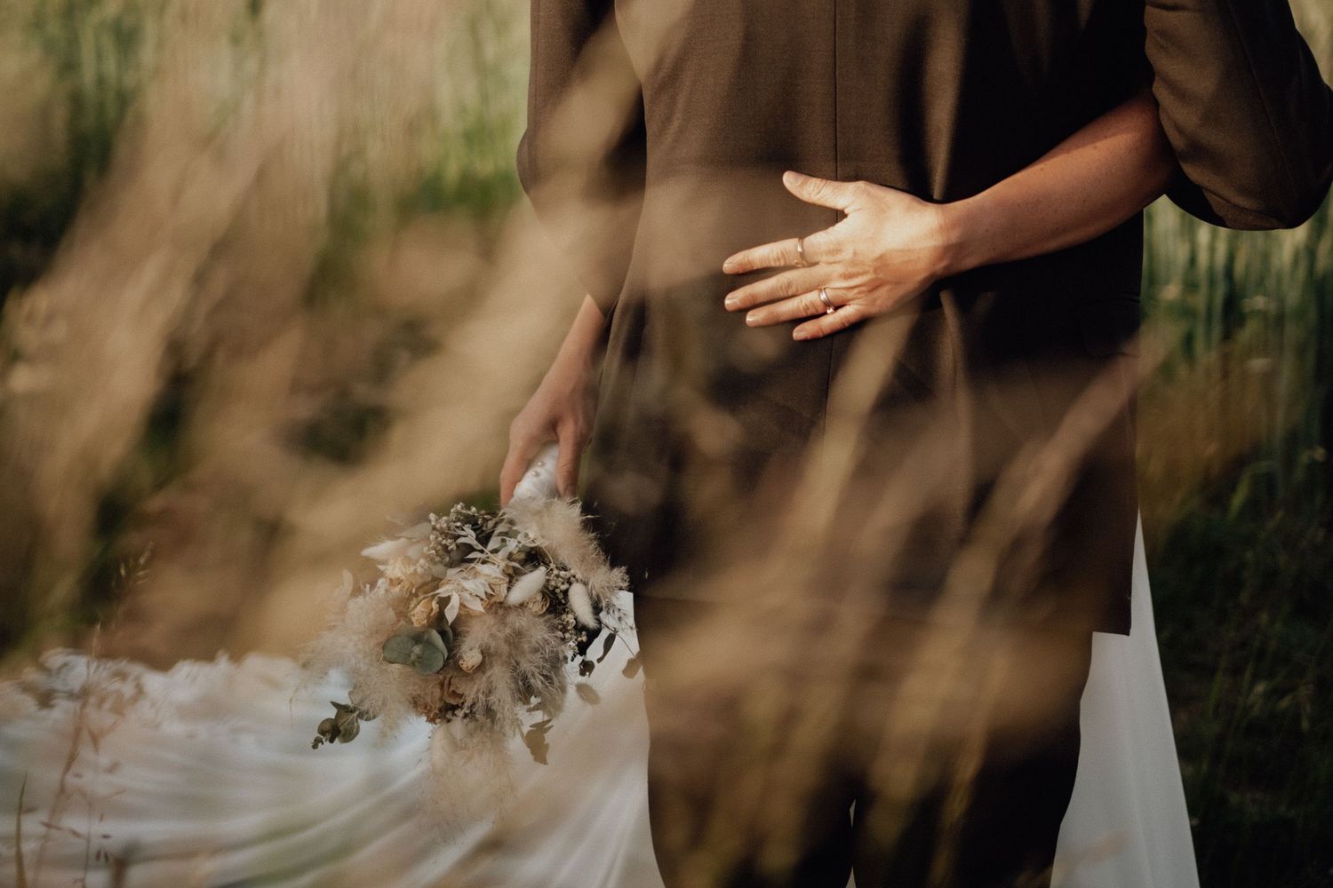 Close up of hands embracing during golden hour with elegant wedding attire visible in soft natural lighting.