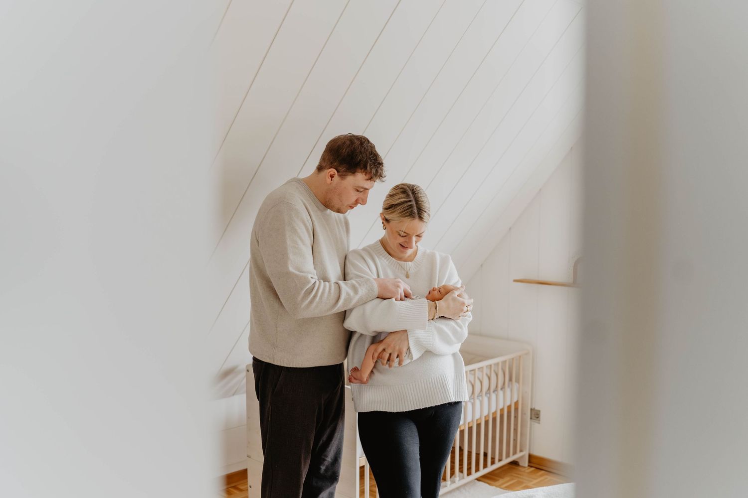 A couple standing in a nursery looking down at their newborn with love.