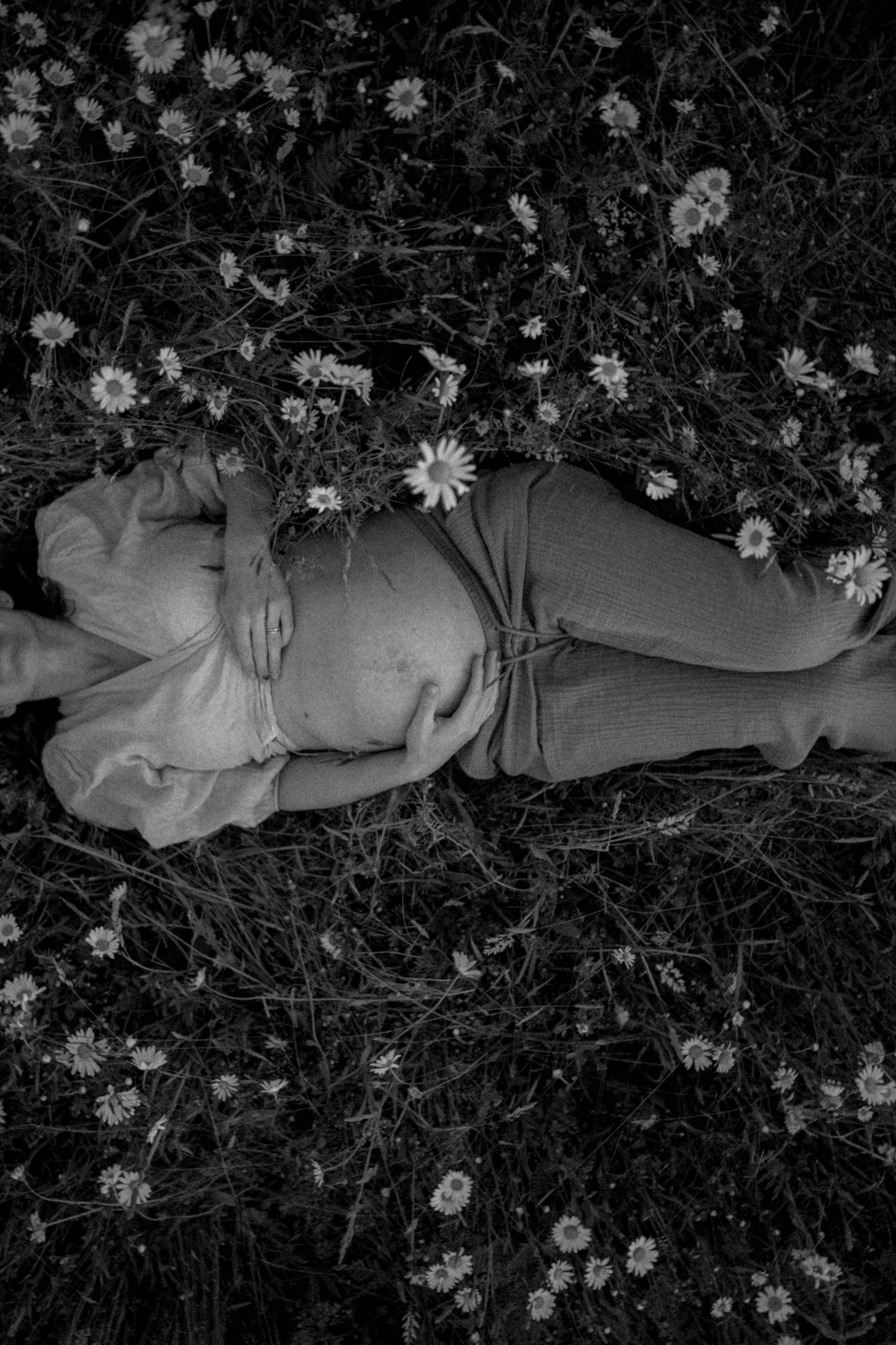 A black and white photo shows a figure resting in a field of daisies.