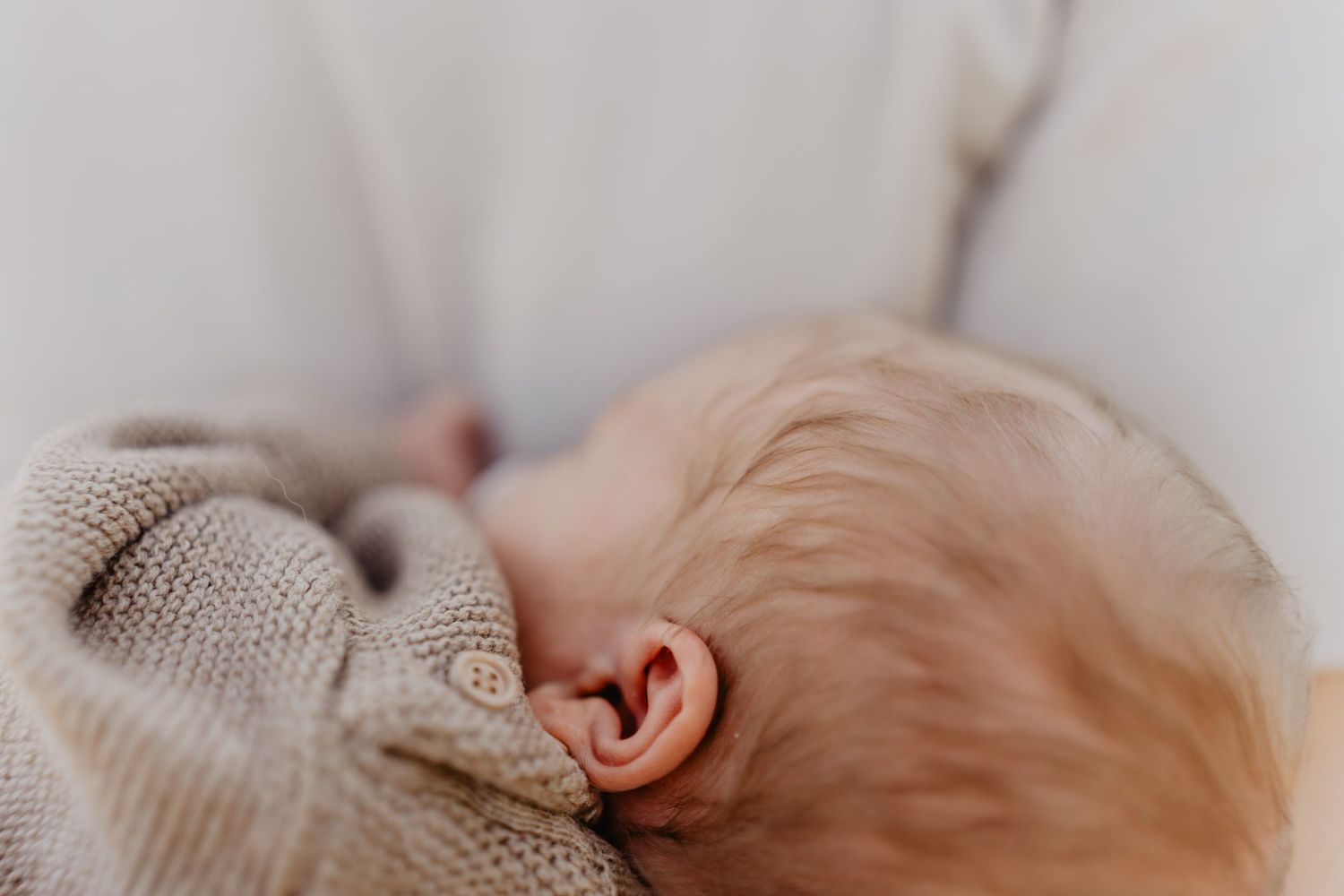 Close up view of a small ear and blonde hair against white knitted fabric background in soft light.