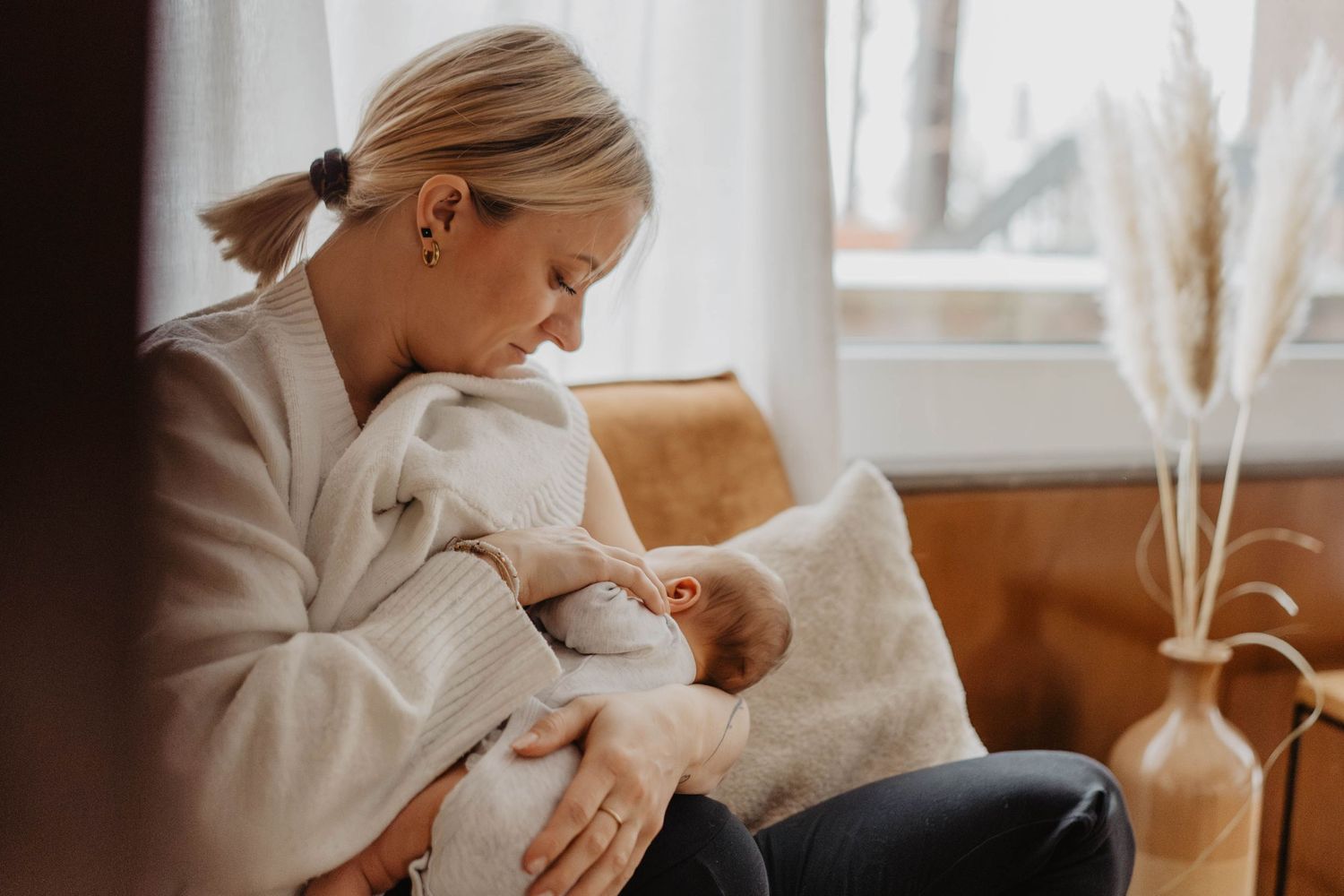Parent in cream sweater nurturing newborn in peaceful living room setting.