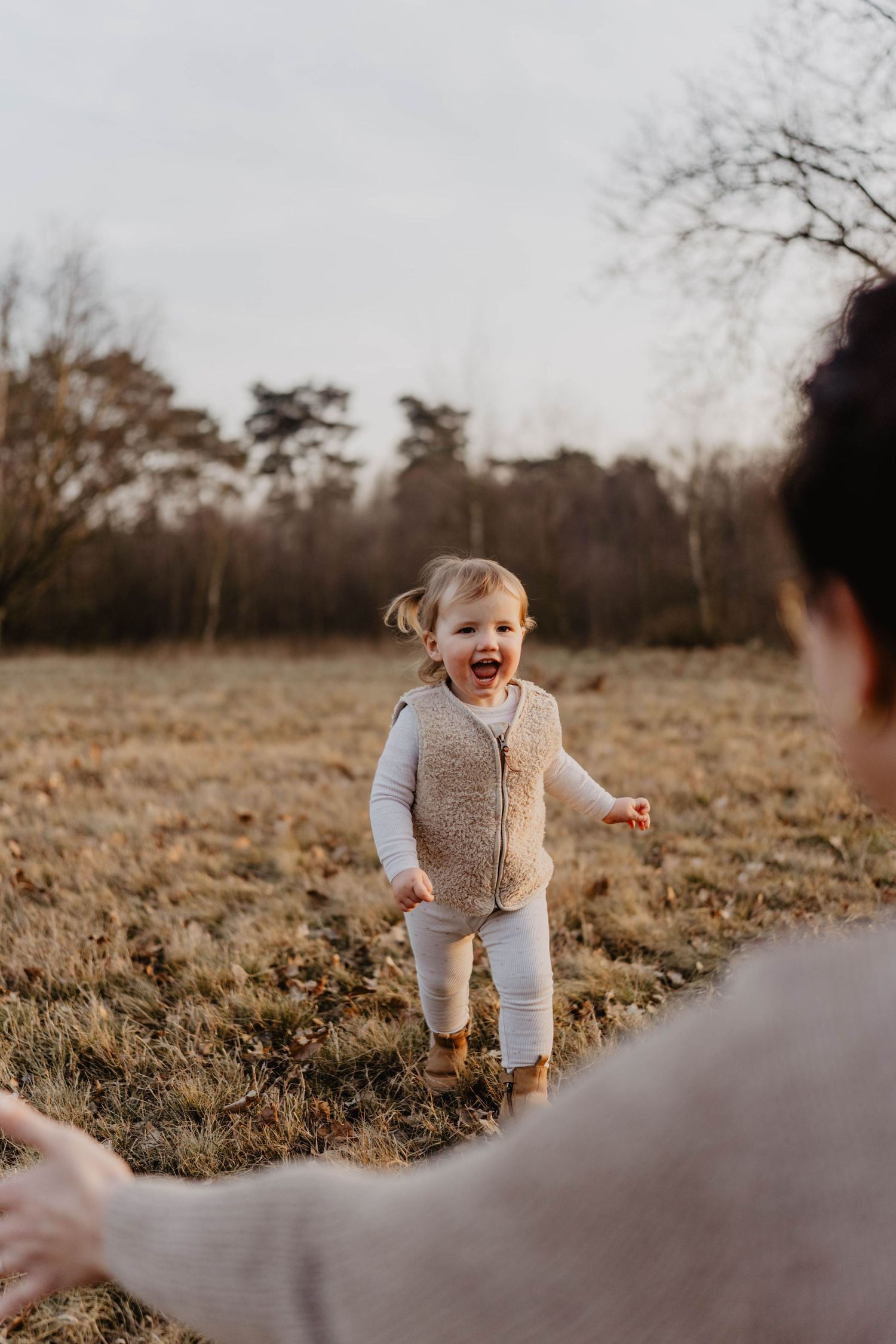A joyful toddler in a beige vest and white pants runs across a golden autumn field at sunset.