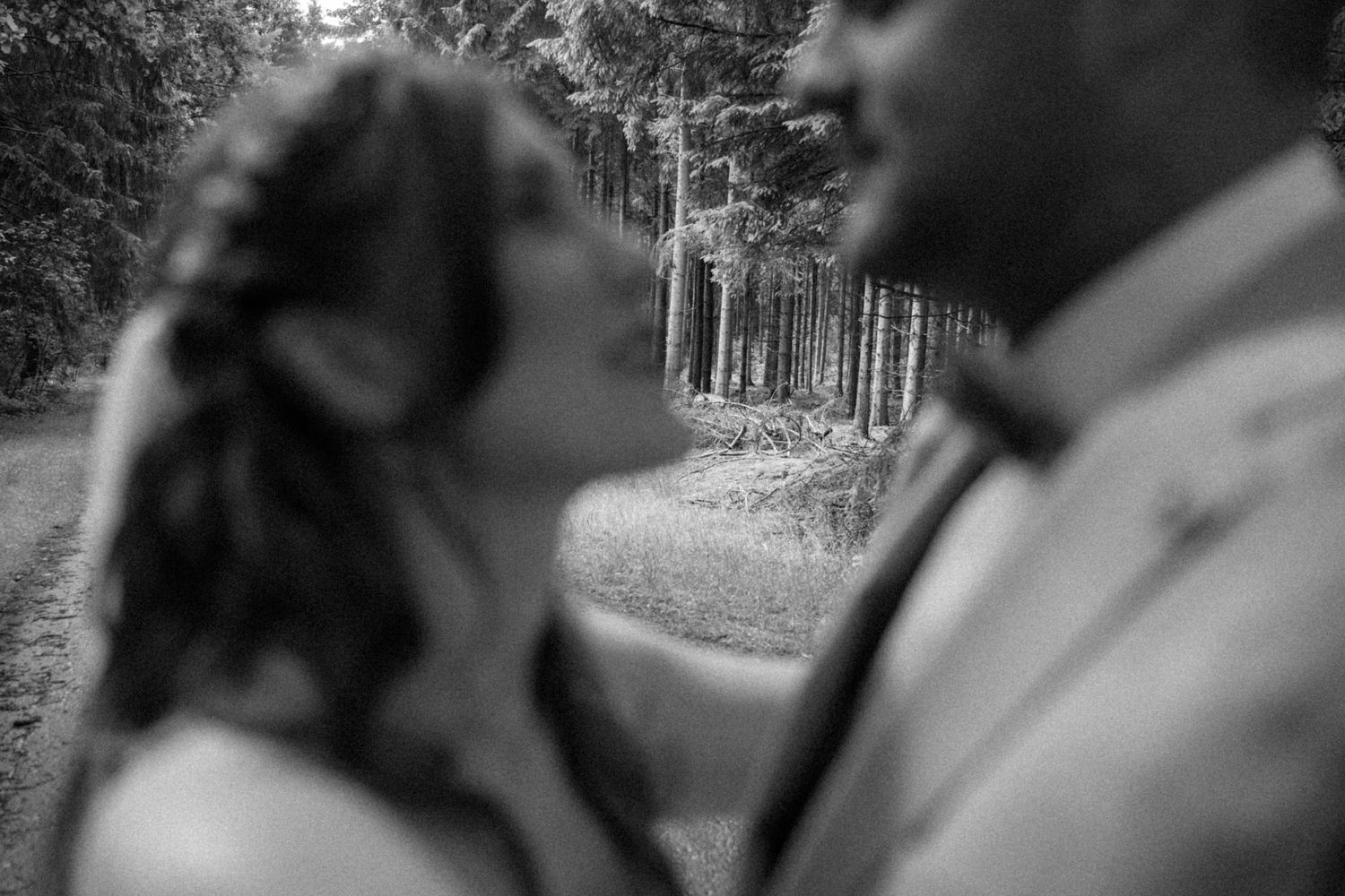 An intimate black and white wedding portrait showing two people in a tender moment outdoors with trees in background.