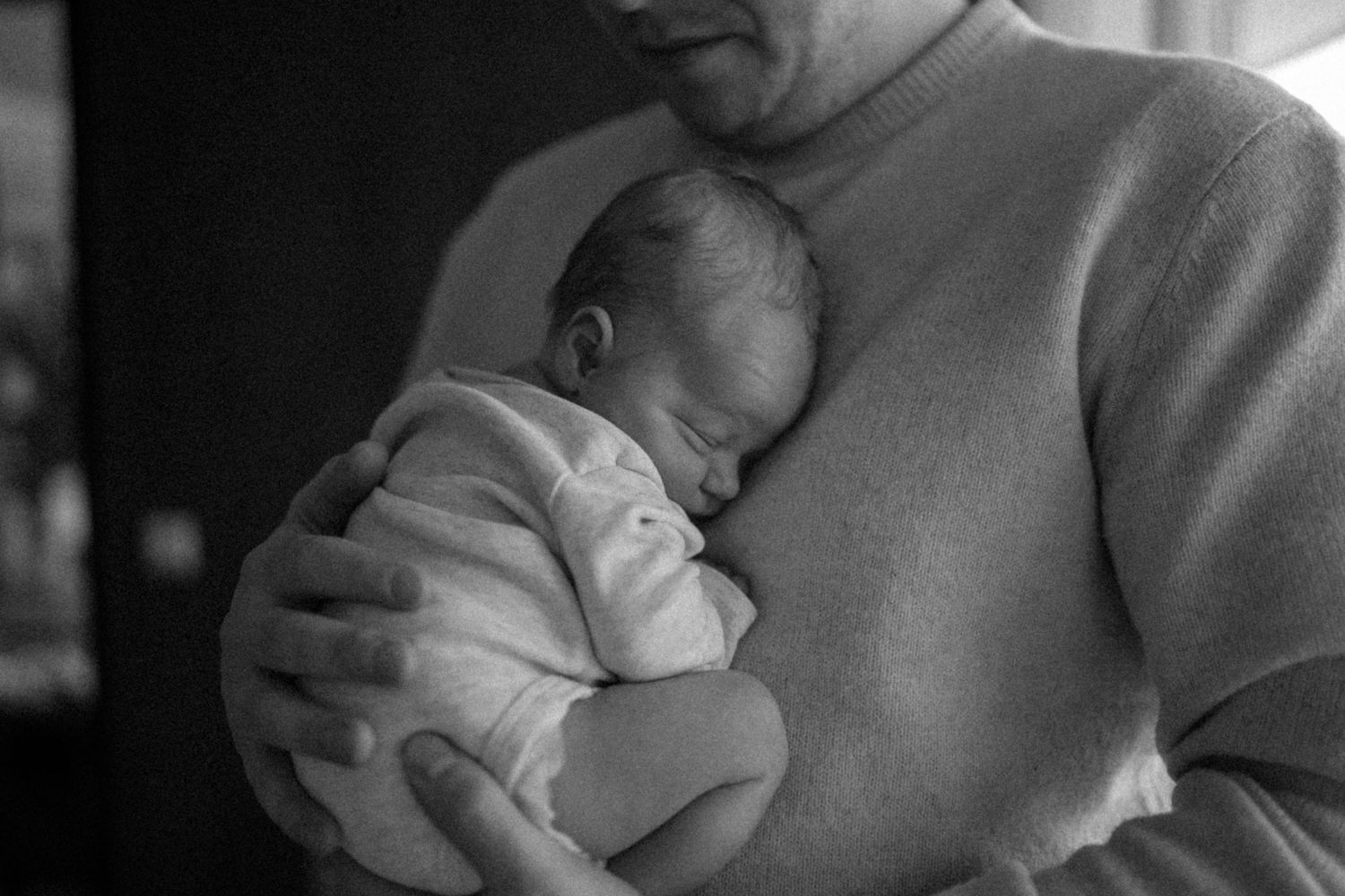 Black and white image of parent cradling sleeping newborn in soft sweater.