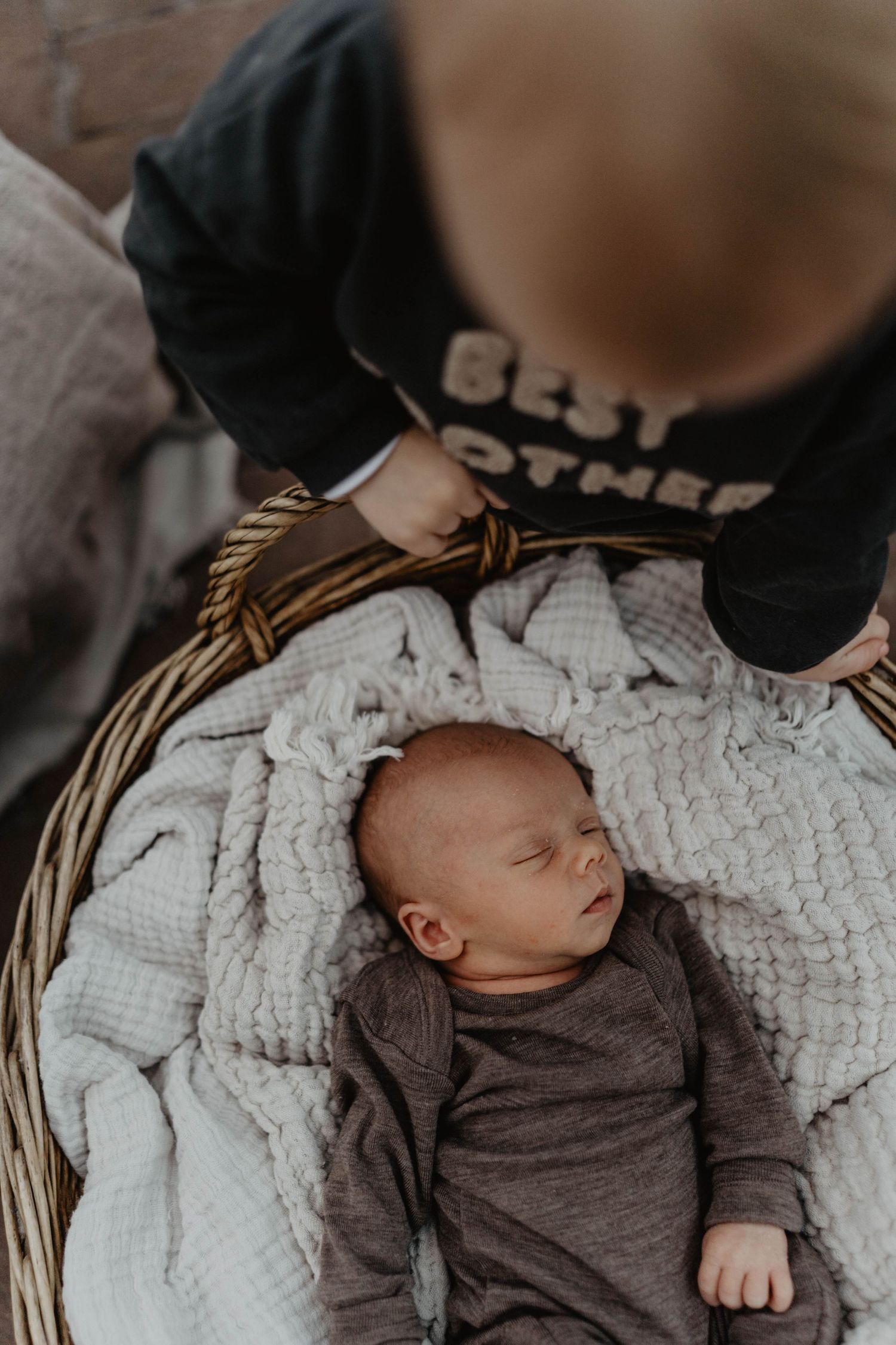 Sleeping infant in gray outfit nestled in white-lined wicker basket.