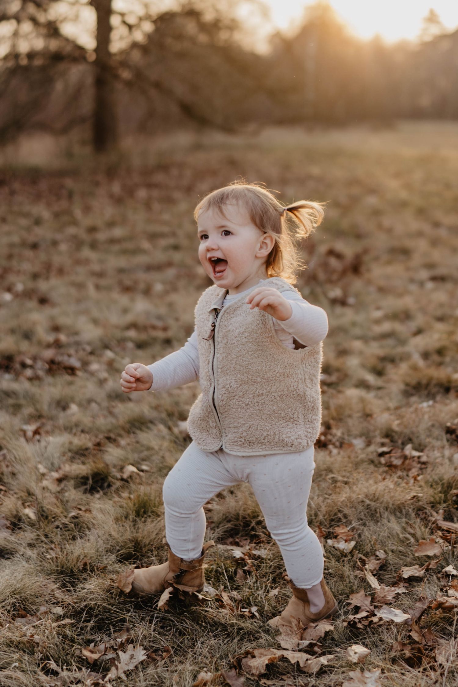 A laughing child in a cozy sherpa vest runs through fallen leaves at golden hour.